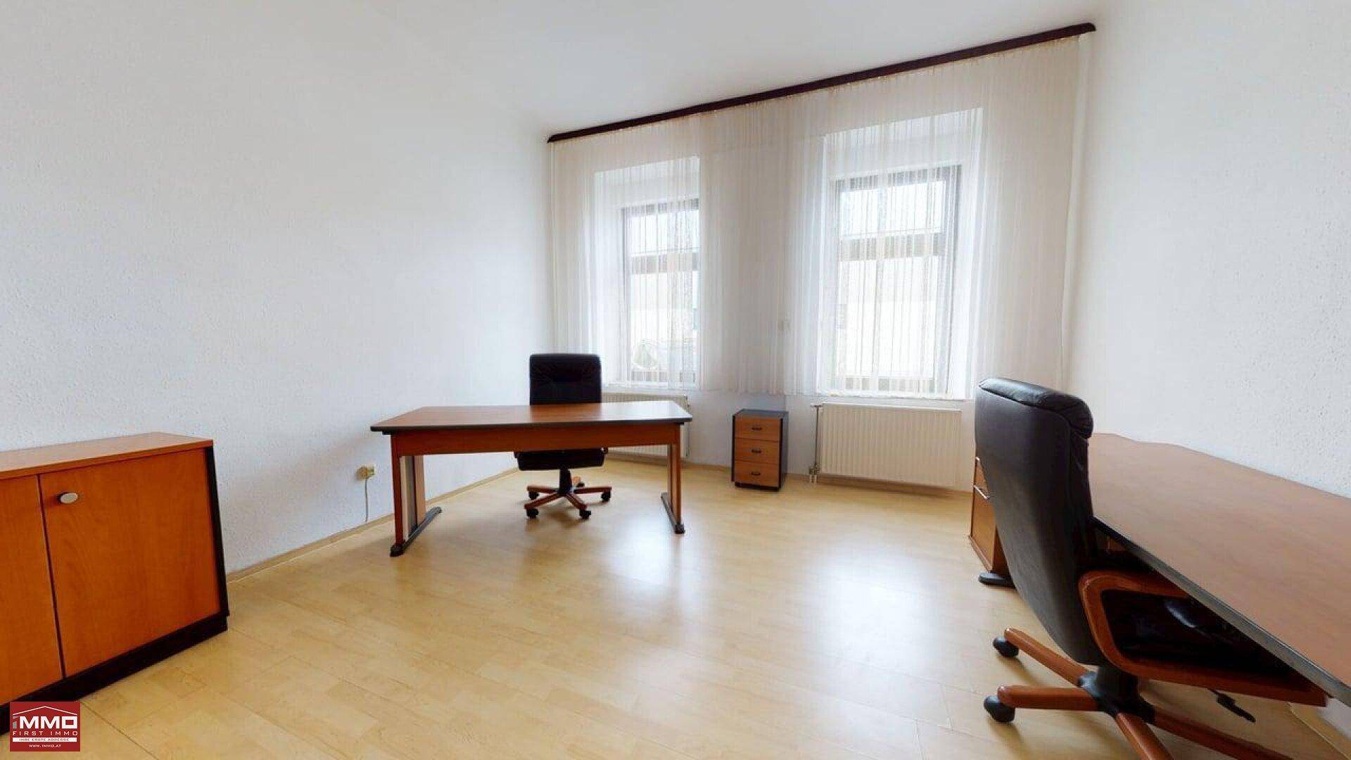 Geräumiges Büro mit Holzfußboden, zwei Fenstern mit Vorhängen und einem Schreibtisch mit Bürostuhl.