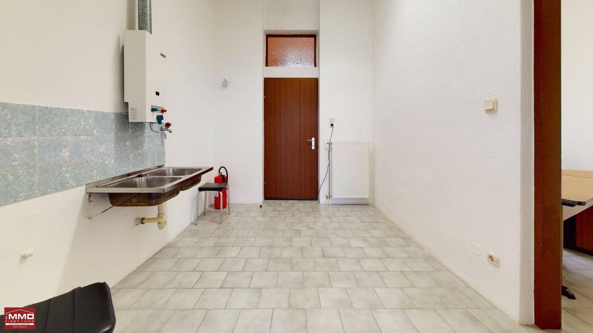 Zweckmäßiger Raum mit Doppelspülbecken, Warmwasserbereiter, gefliester Rückwand und einer Tür.