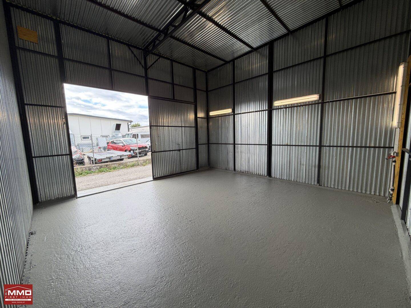 Geräumige Lagerhalle mit offener Tür, die Tageslicht hereinlässt, und einem robusten Betonboden.