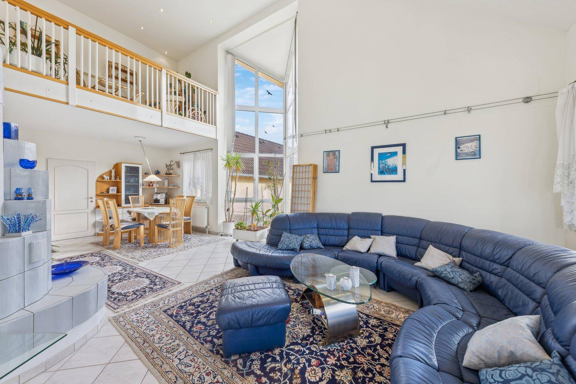 Helles Wohnzimmer mit hohen Decken, großen Fenstern und einer Galerie, die den Raum öffnet.