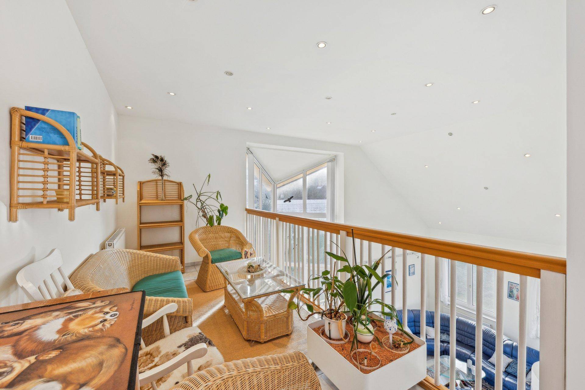 Helle Galerie mit Rattanmöbeln und Blick auf den darunterliegenden Wohnbereich, ideal zum Entspannen.