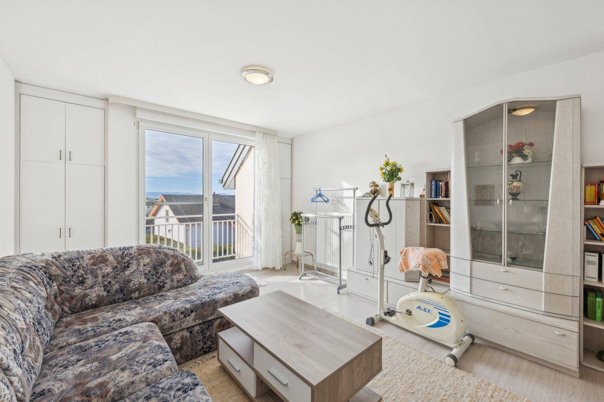 Helles Zimmer mit Balkonzugang, Einbauschränken und einem Fitnessgerät, vielseitig nutzbar.