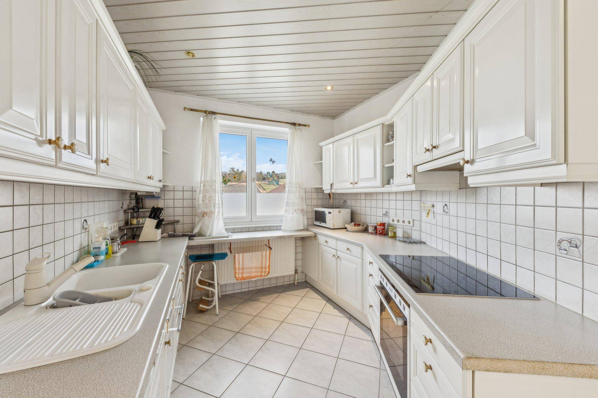 Traditionelle weiße Küche mit Einbauschränken, Fliesenboden und einem Fenster mit Blick nach draußen.