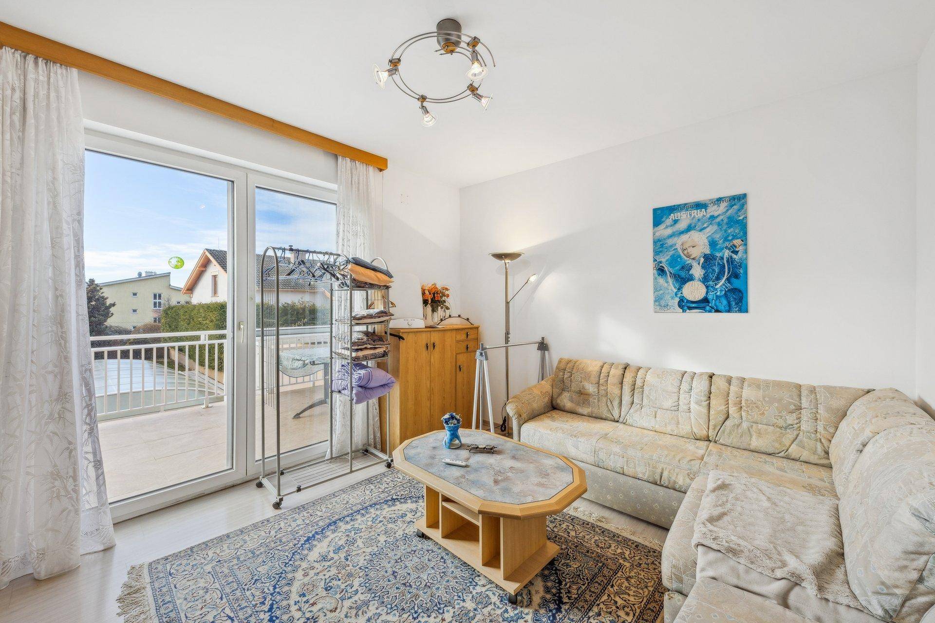 Gemütliches Wohnzimmer mit Zugang zu einem Balkon, hellem Laminatboden und einem bequemen Sofa.