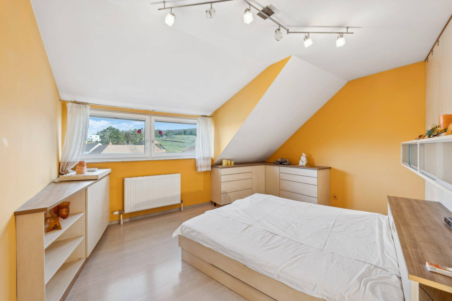 Helles Schlafzimmer im Dachgeschoss mit gelben Wänden, Dachschrägen und weitem Blick in die Landschaft.