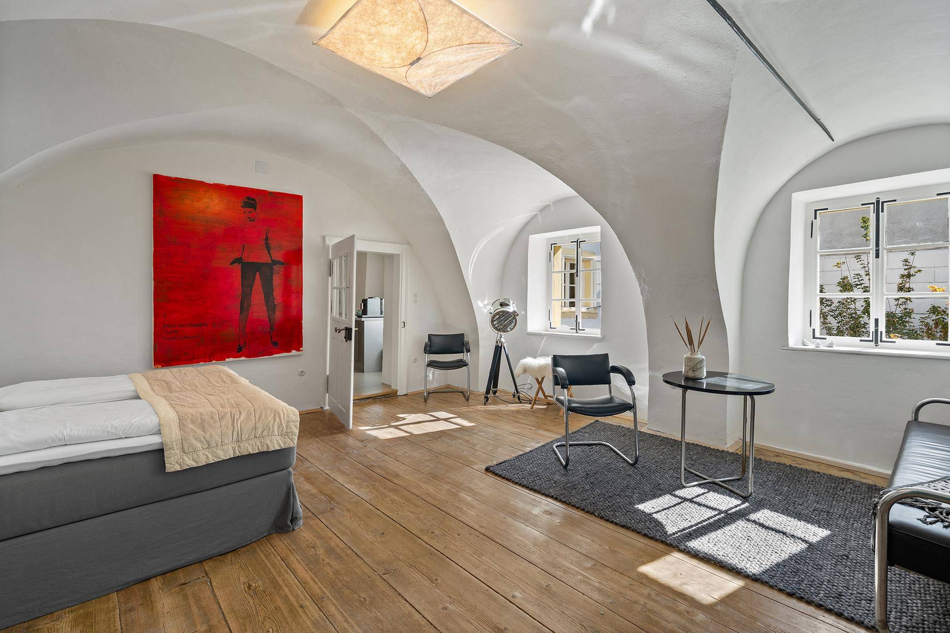Helles Schlafzimmer mit Gewölbedecke, Holzdielenboden und moderner Kunst an der Wand.