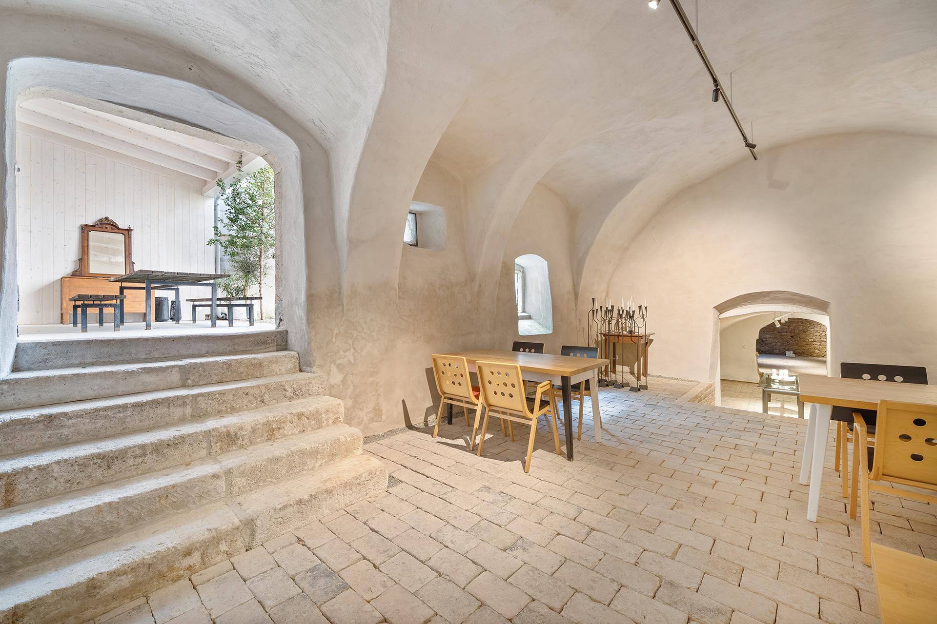 Historischer Gewölbegang mit Steinboden und Treppe, führt zu einem überdachten Außenbereich.