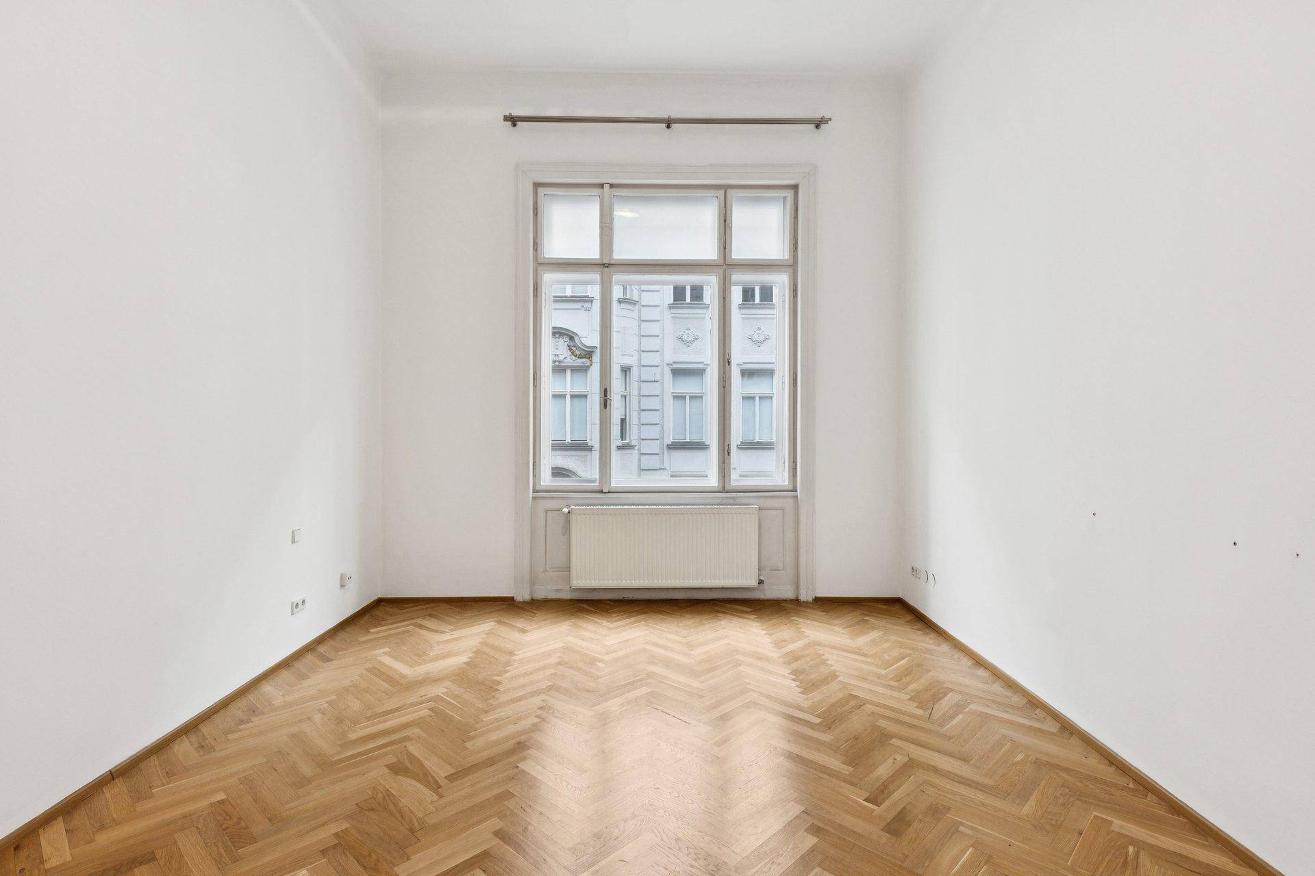 Helles Zimmer mit Fischgrätparkett und großem Fenster, ideal als Schlafzimmer.