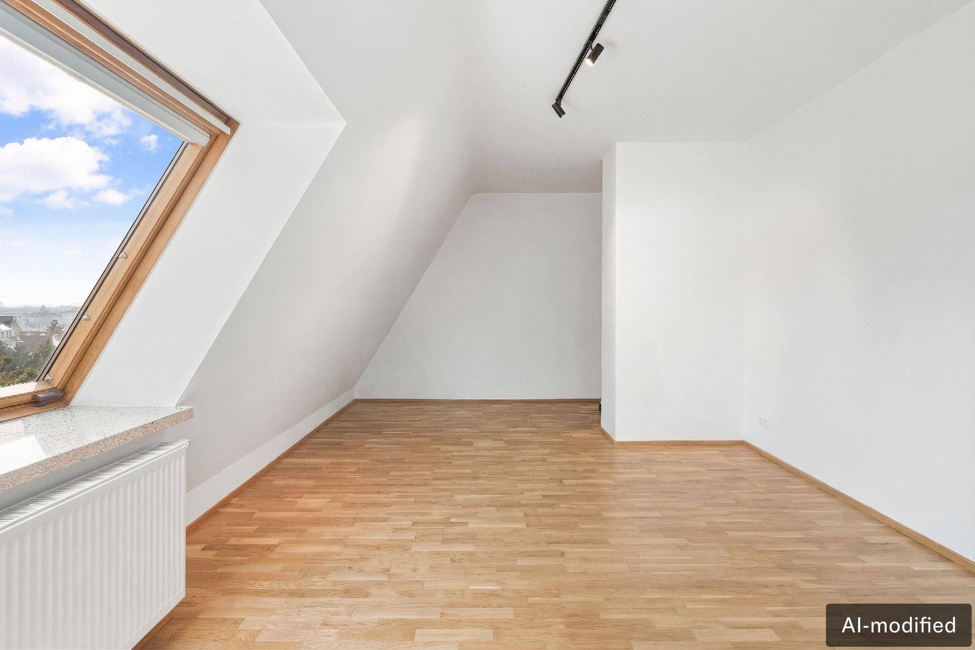 Heller, leerer Raum mit Holzboden und großem Dachfenster.