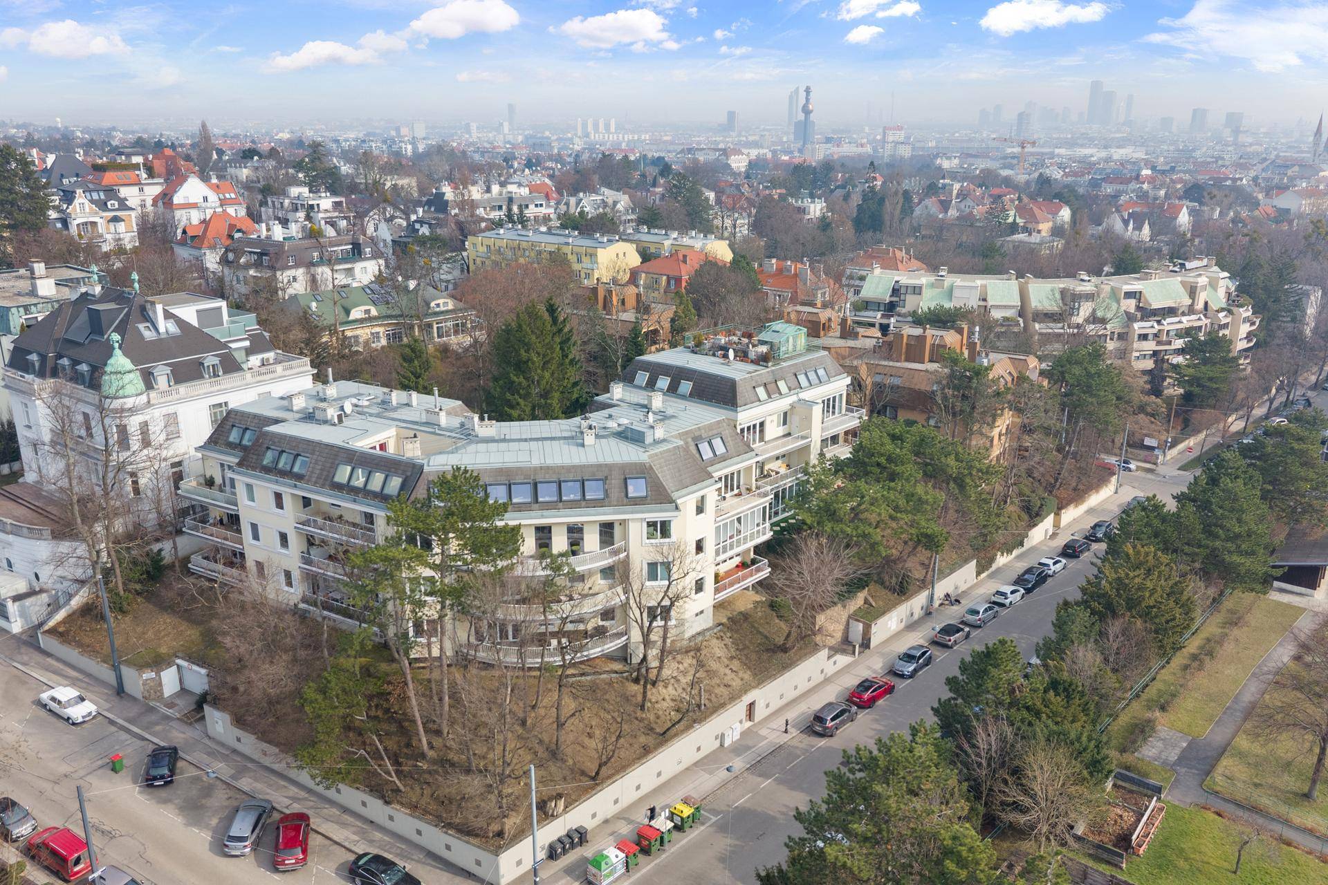 Luftaufnahme eines modernen Wohngebäudes in einer grünen Umgebung mit Stadtblick.