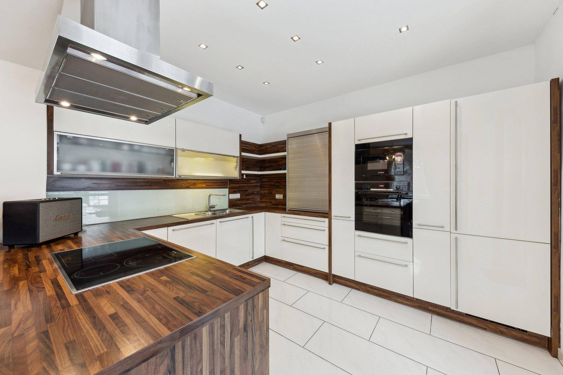 Moderne Küche mit weißen Hochglanzfronten, Holz-Arbeitsplatten und integrierten Geräten.