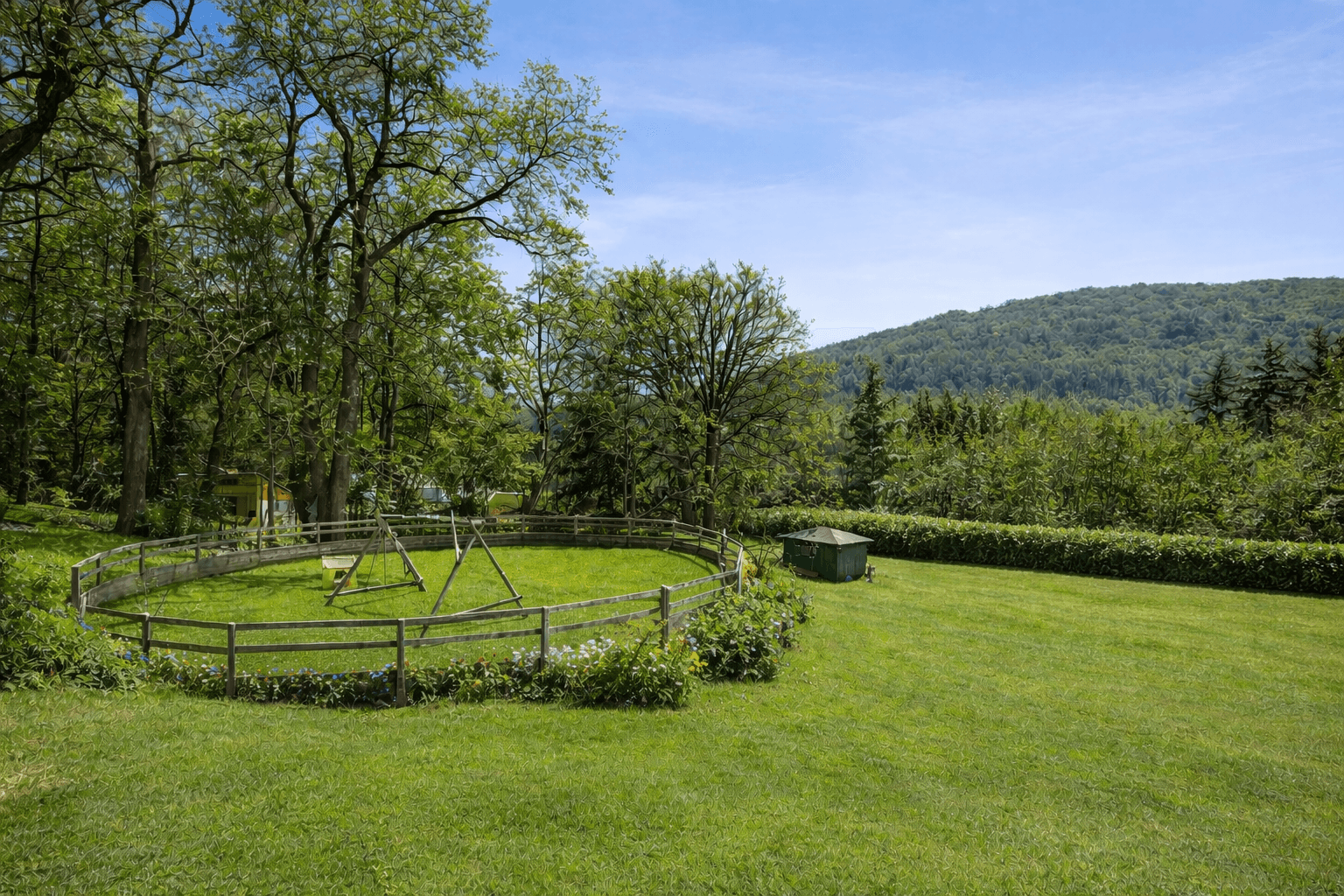 Großer Gartenbereich mit Schaukeln und viel Grün, umgeben von Bäumen und Hügeln.