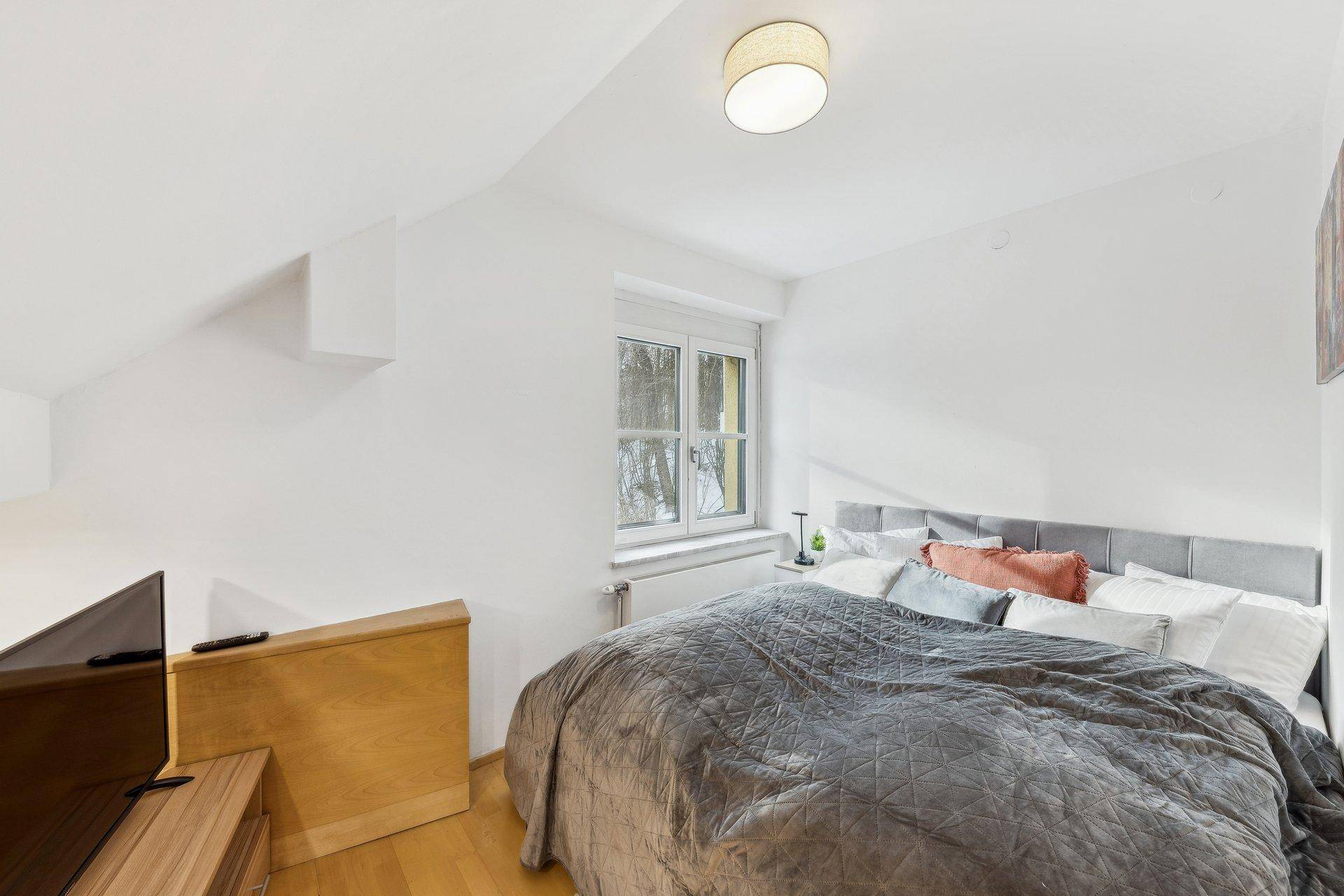 Gemütliches Schlafzimmer im Dachgeschoss mit Holzboden, Schrägen und einem Fenster.
