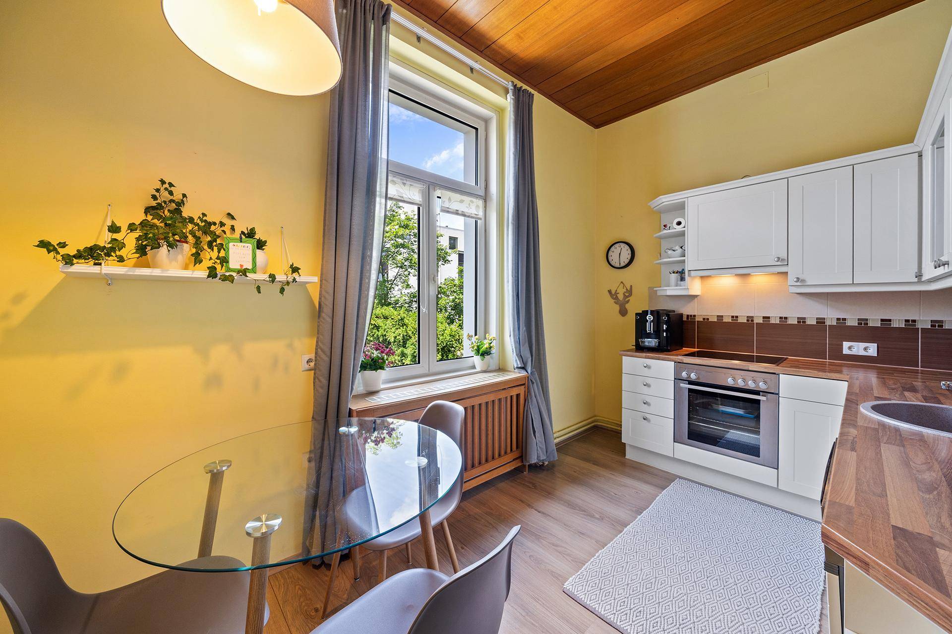 Gemütliche Küche mit gelben Wänden, Holzbalkendecke und Essbereich am Fenster.