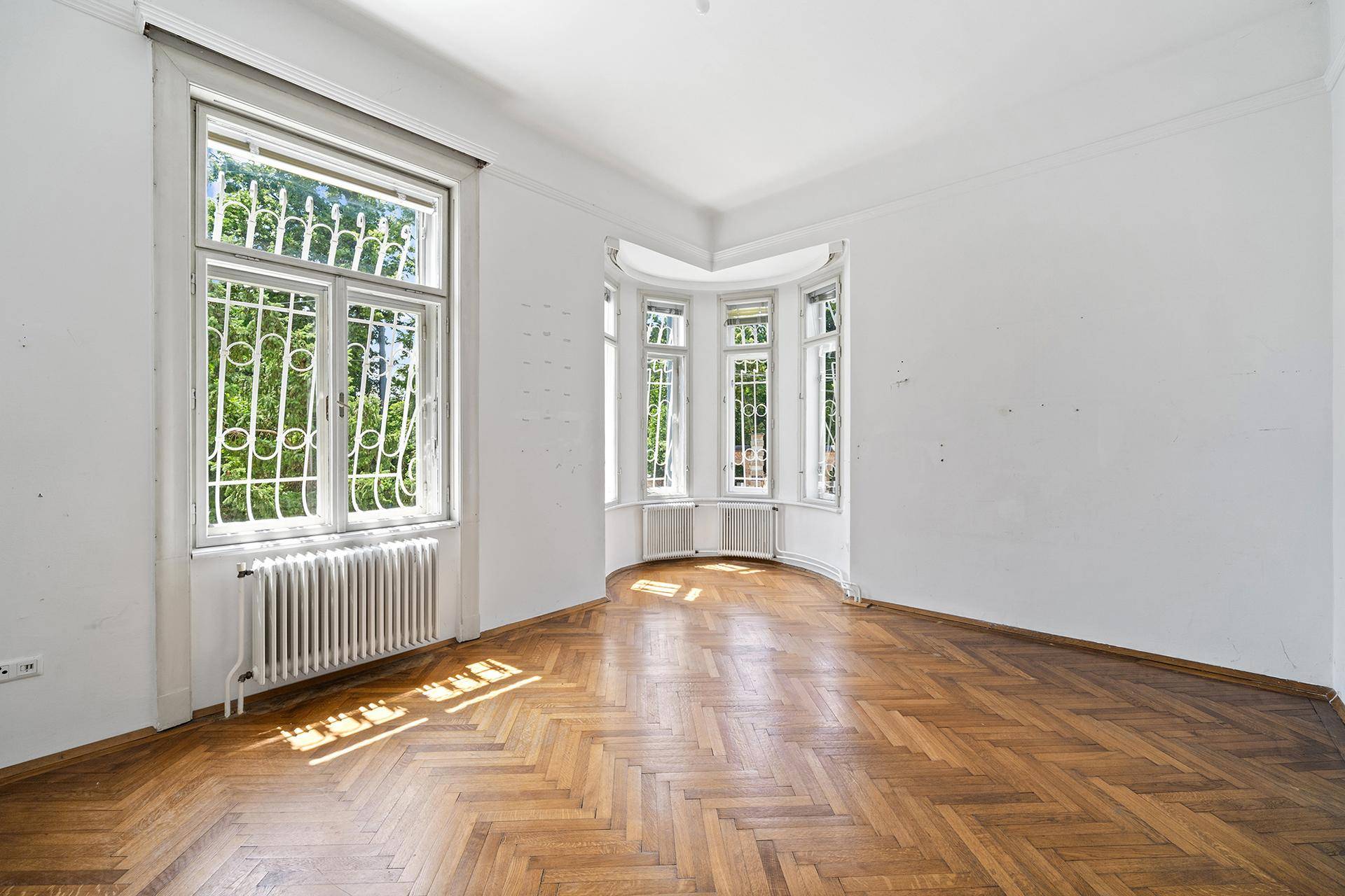 Helles Wohnzimmer mit Erkerfenstern, Fischgrätparkett und Blick ins Grüne.
