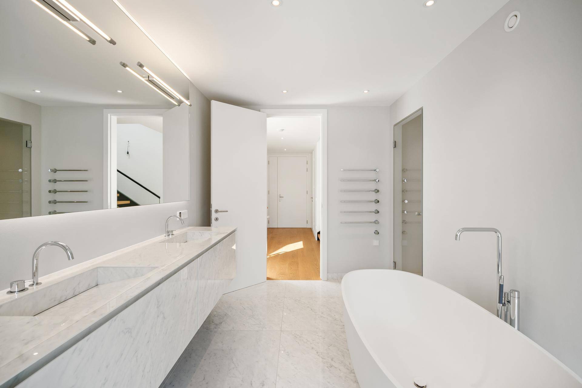Modernes Badezimmer mit Doppelwaschbecken, freistehender Badewanne und Handtuchheizkörper.