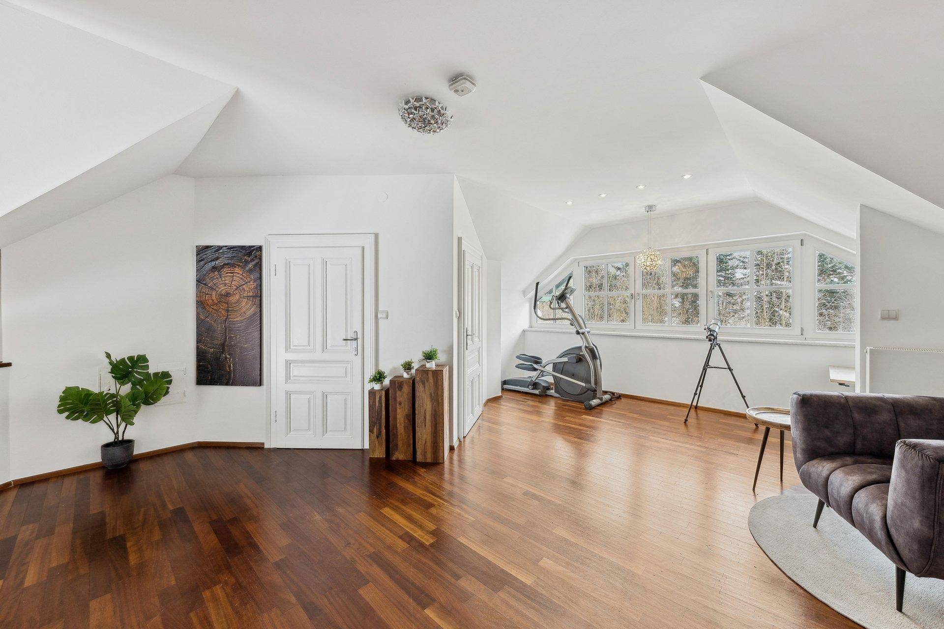 Geräumiger Dachbodenraum mit Holzboden, Schrägen und großen Fenstern, ideal als Fitnessbereich.