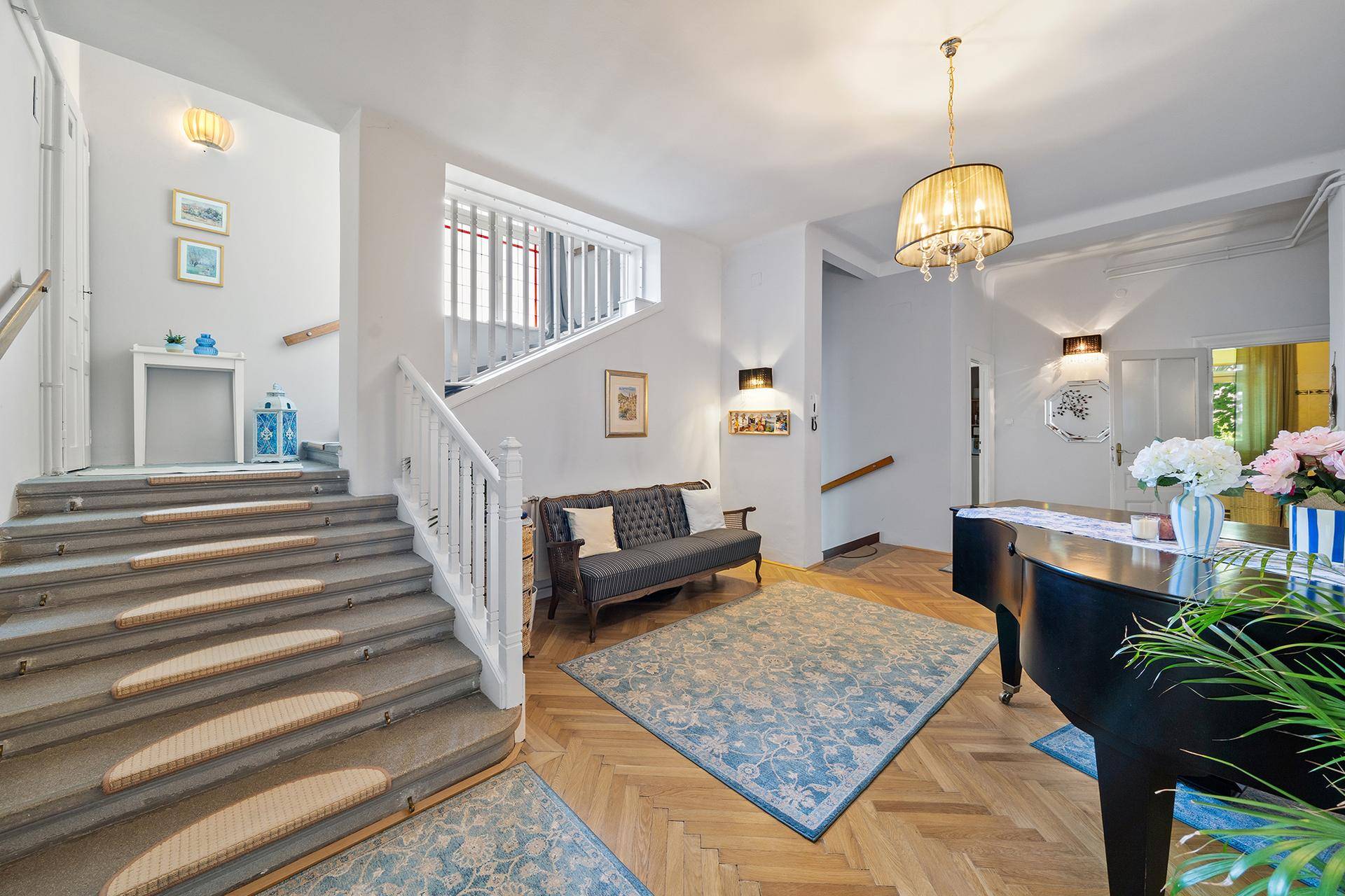 Geräumiger Eingangsbereich mit Holzparkett, Treppe und einem Flügel.
