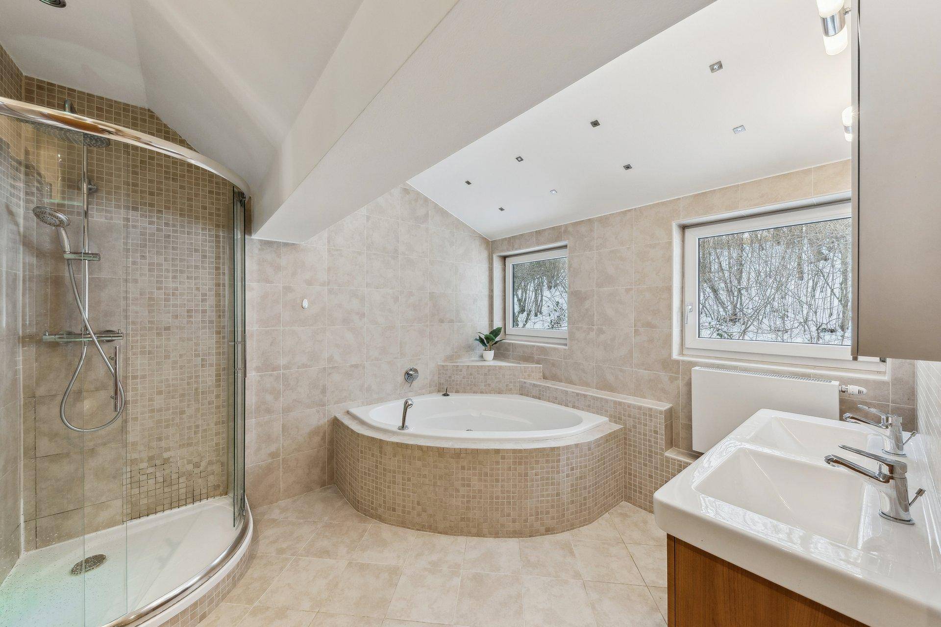 Geräumiges Badezimmer mit Eckbadewanne, Dusche und Doppelwaschbecken in hellen Fliesen.