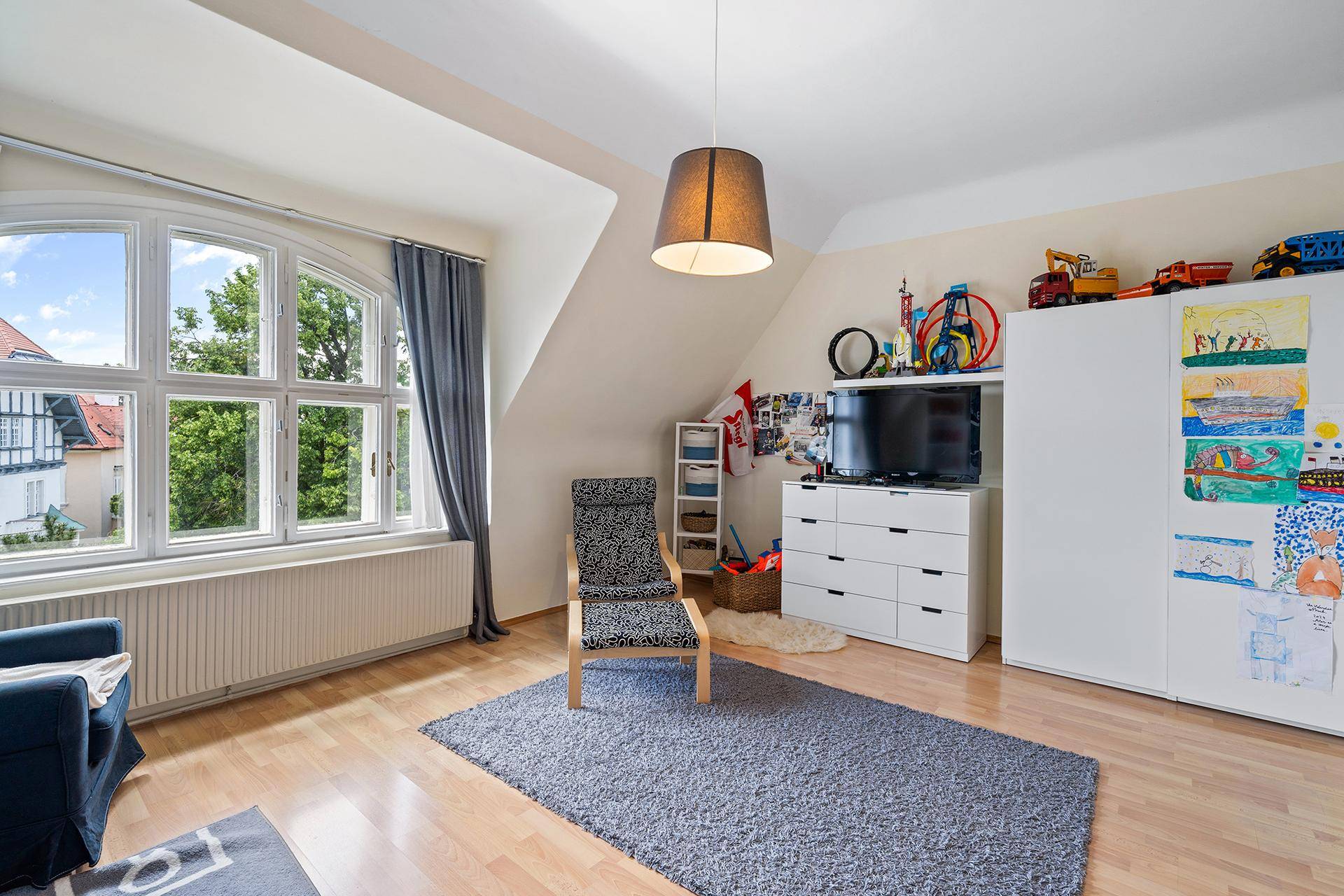 Kinderzimmer mit Dachschräge, Laminatboden und großem Fenster mit Stadtblick.