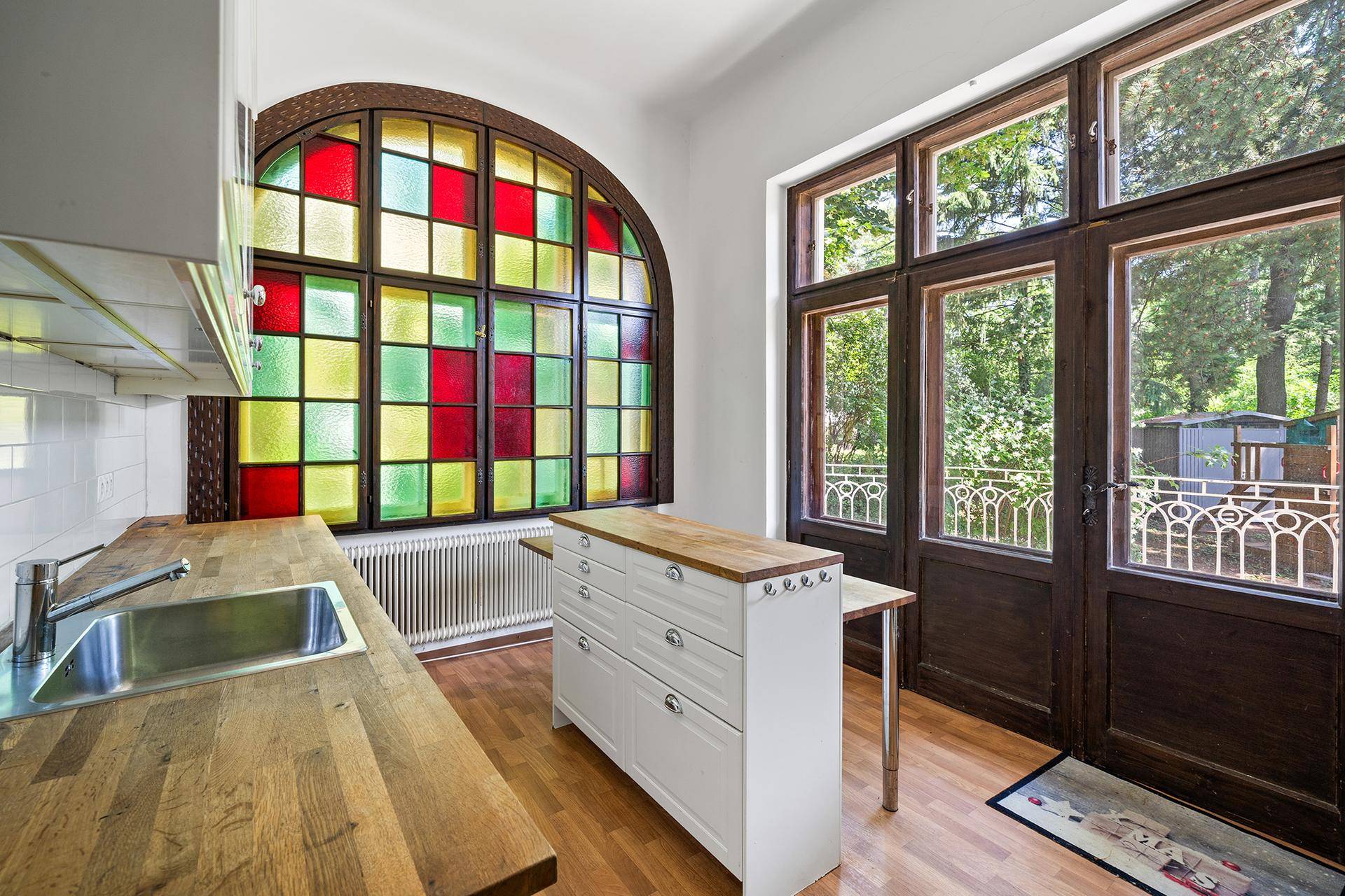 Küche mit Holzarbeitsplatten, farbigen Bleiglasfenstern und Zugang zu einem kleinen Balkon.