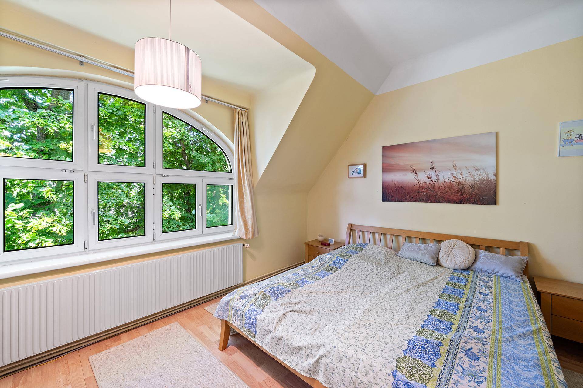 Schlafzimmer mit Holzbett, Laminatboden und großem Fenster mit Blick ins Grüne.