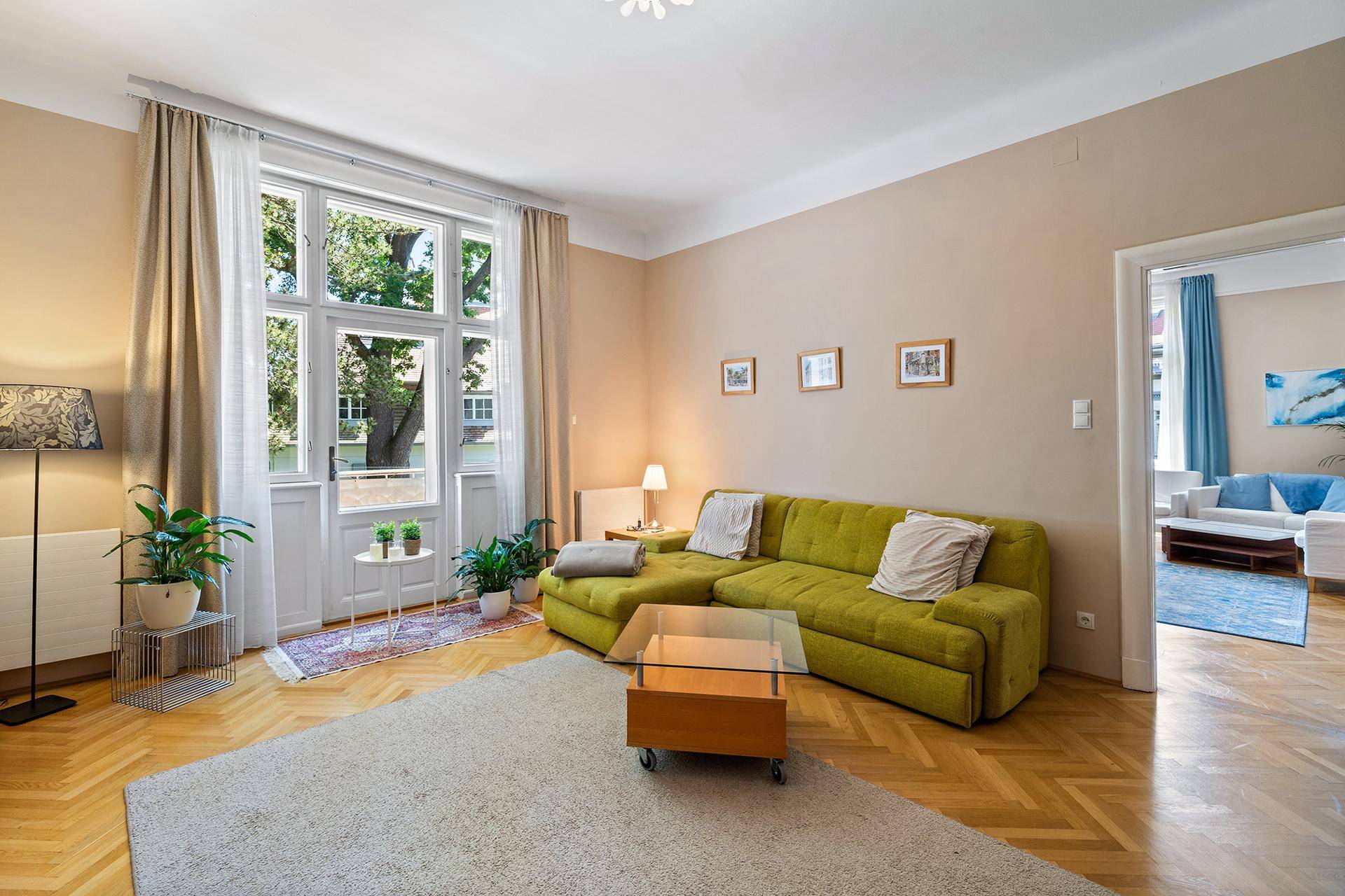 Helles Wohnzimmer mit grünem Ecksofa, Fischgrätparkett und Zugang zum Balkon.