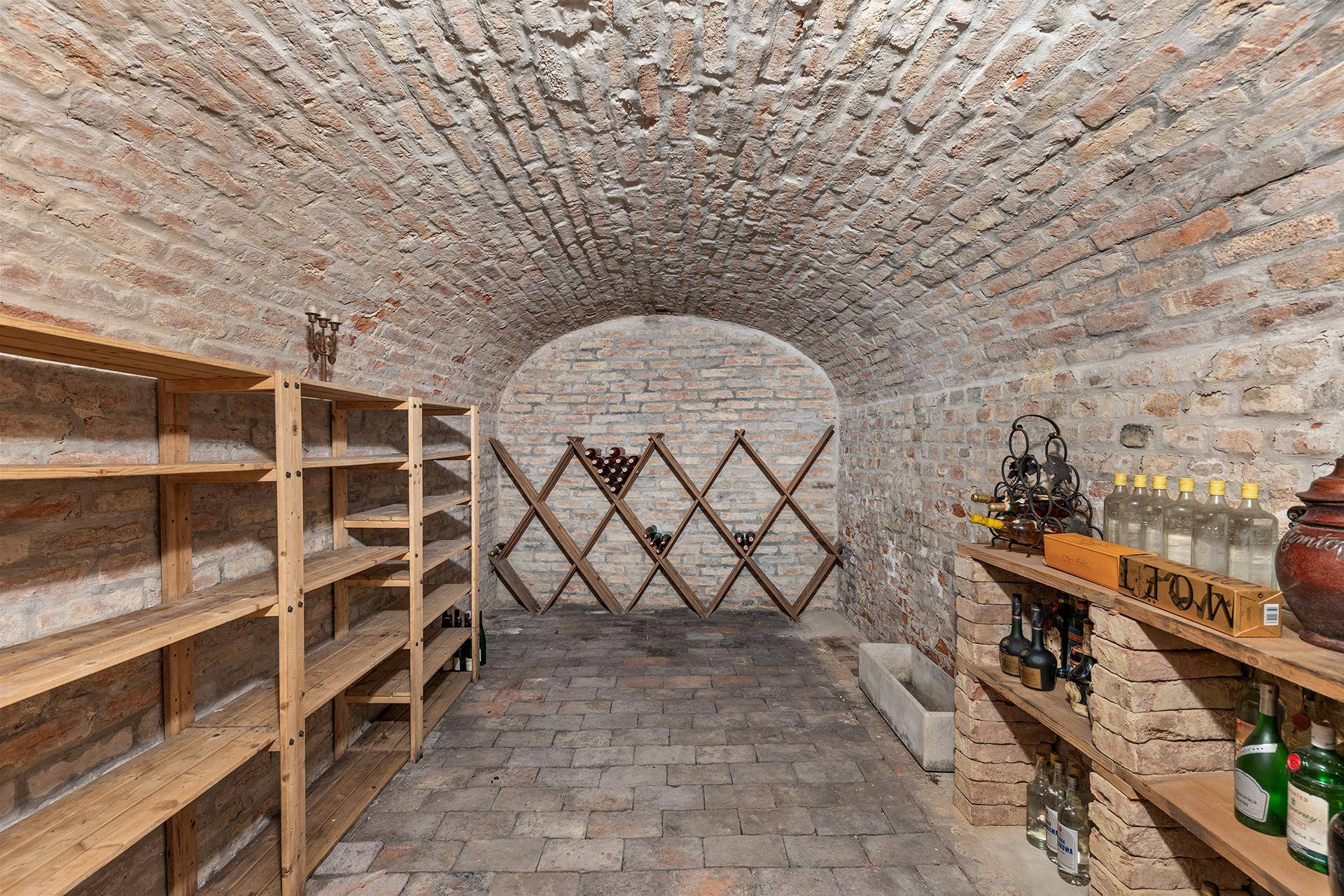 Historischer Weinkeller mit Ziegelgewölbe, Holzregalen und gelagerten Weinflaschen.