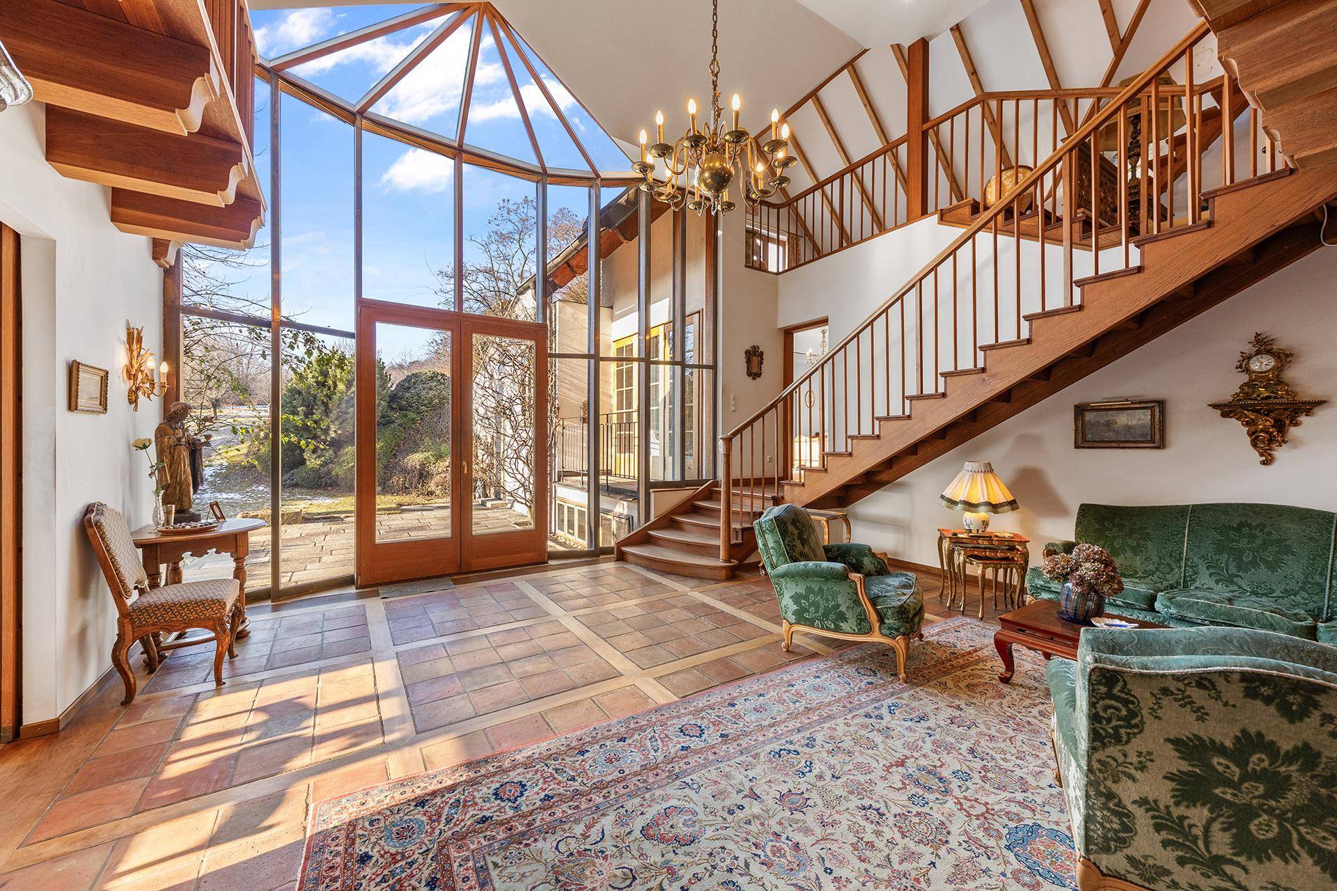 Großzügiger Eingangsbereich mit hohen Glasfronten, Holztreppe und eleganten Sitzgelegenheiten.