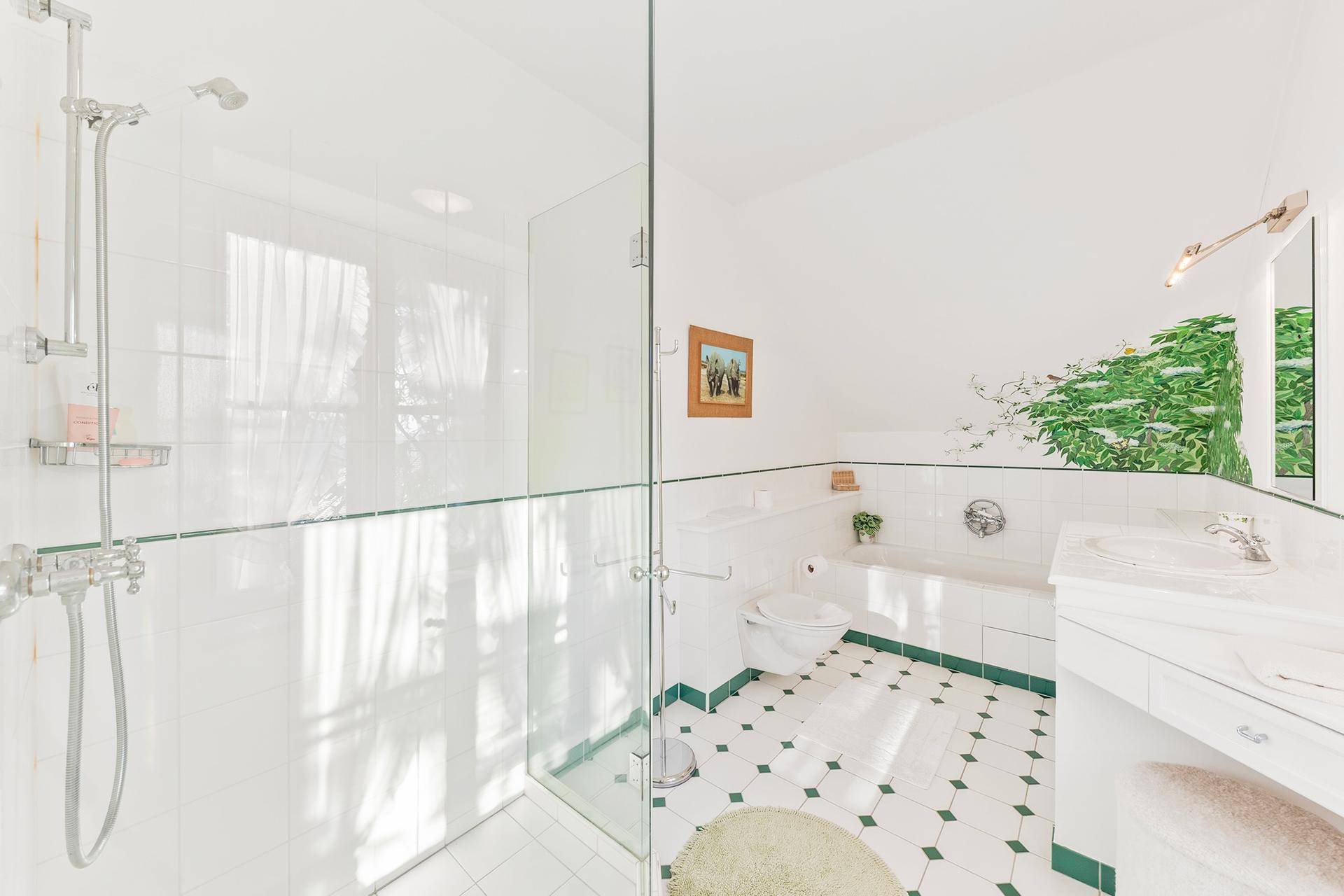 Helles Badezimmer mit Duschkabine, Badewanne und grün-weiß gefliestem Boden.