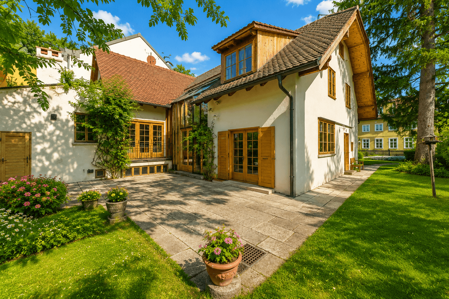 Geräumige Steinterrasse mit Topfpflanzen und Zugang zum Haus, umgeben von einem grünen Garten.