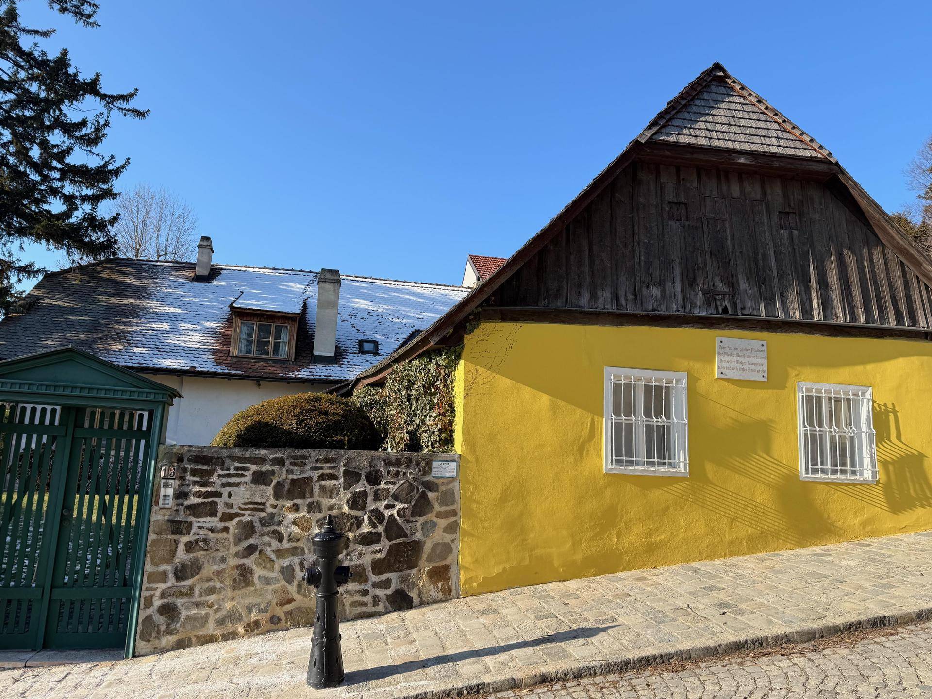 Traditionelles gelbes Haus mit Holzdach und Steinmauer an einer gepflasterten Straße.