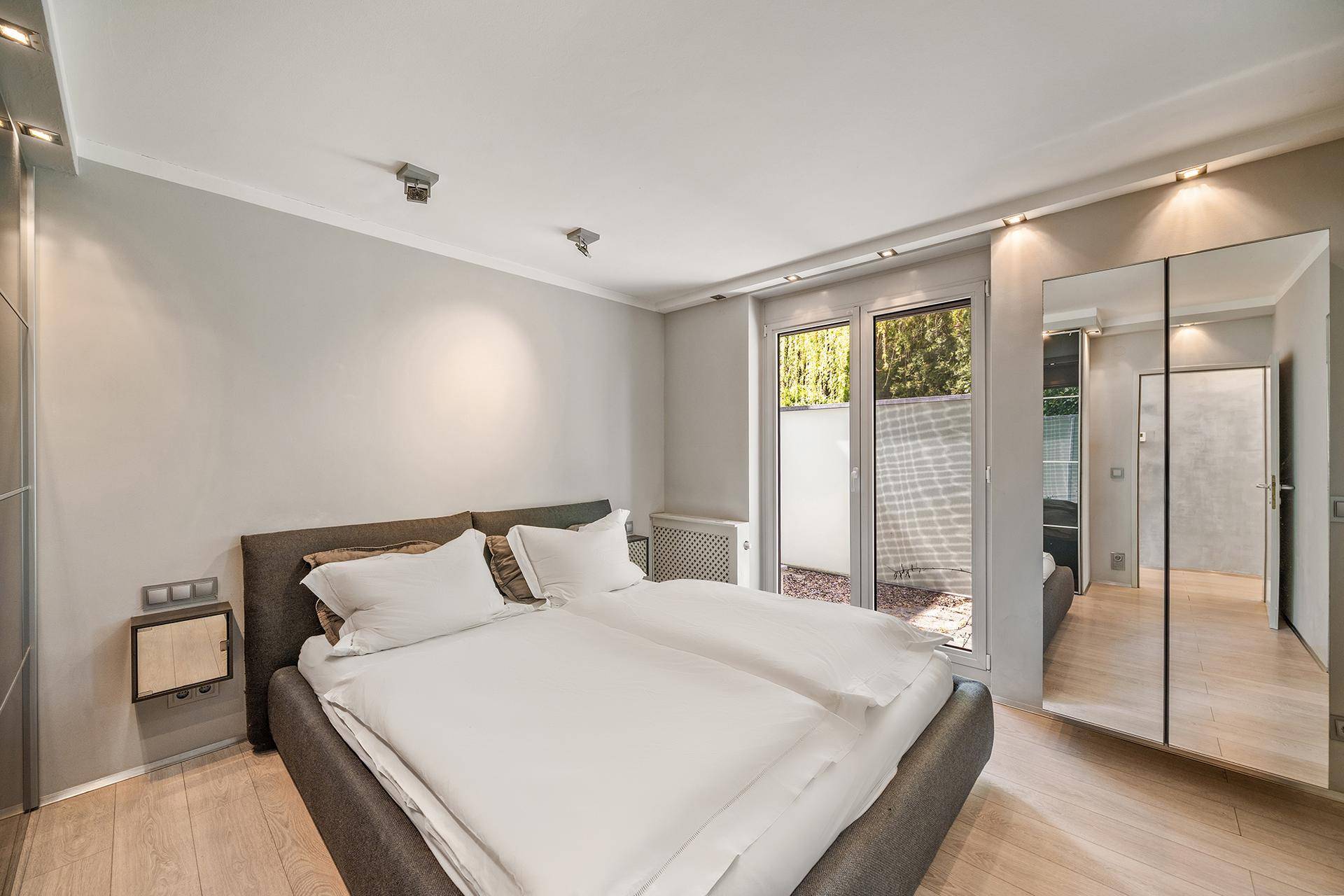 Modernes Schlafzimmer mit Doppelbett, Einbauschränken und Zugang zu einem Außenbereich.
