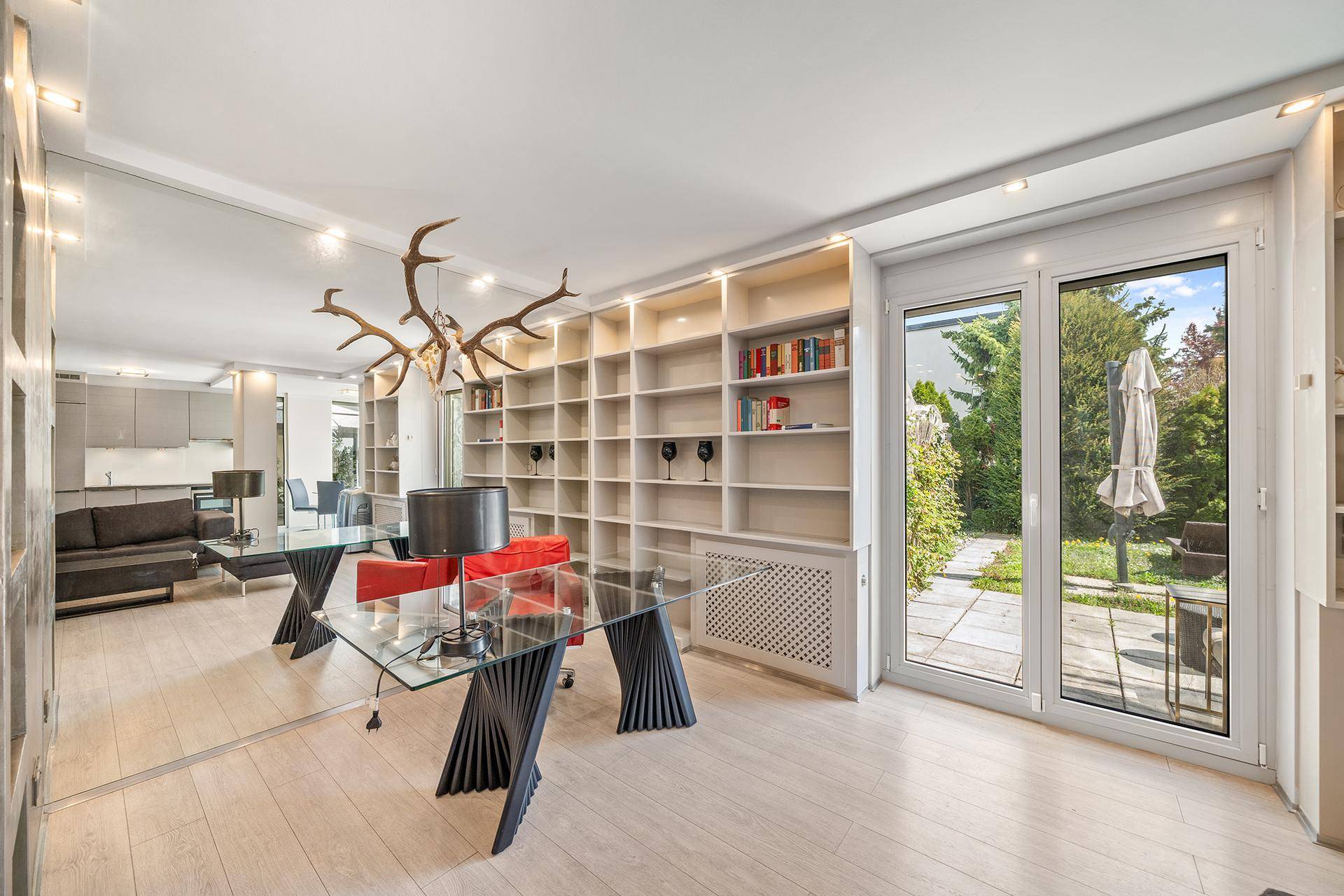 Helles Wohnzimmer mit großem Bücherregal, Arbeitsbereich und direktem Gartenzugang.