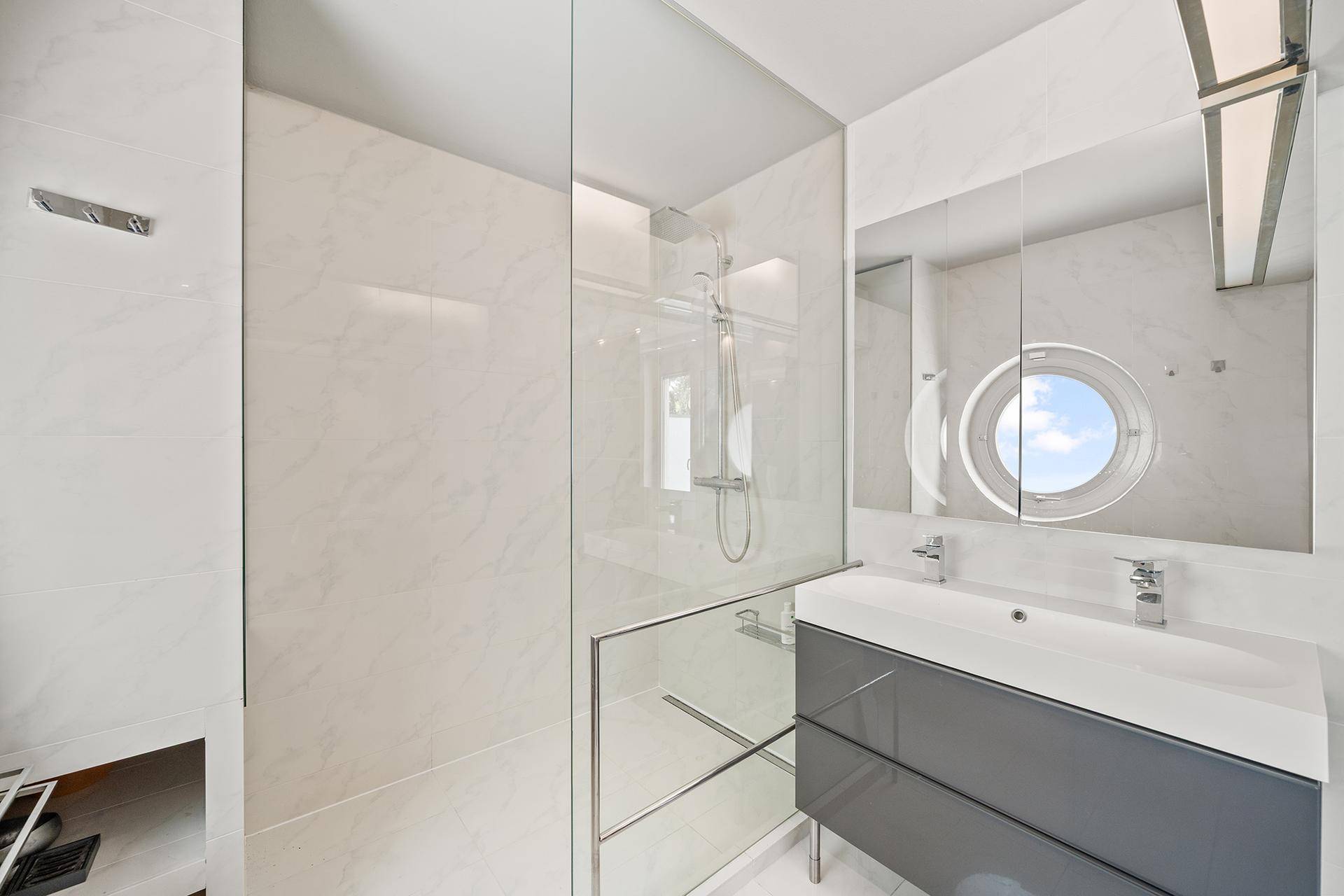 Elegantes Badezimmer mit begehbarer Dusche, Doppelwaschbecken und rundem Fenster.