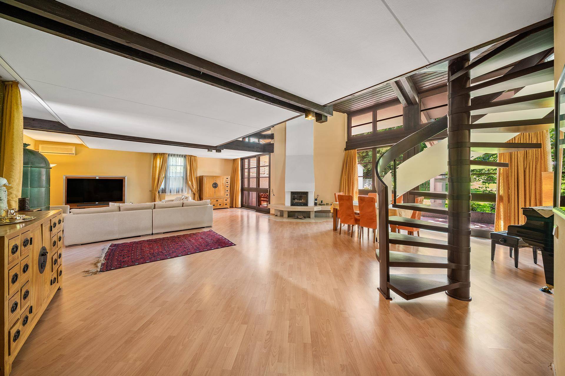 Geräumiger Wohn-Essbereich mit Holzbalken, Kamin und einer eleganten Wendeltreppe.