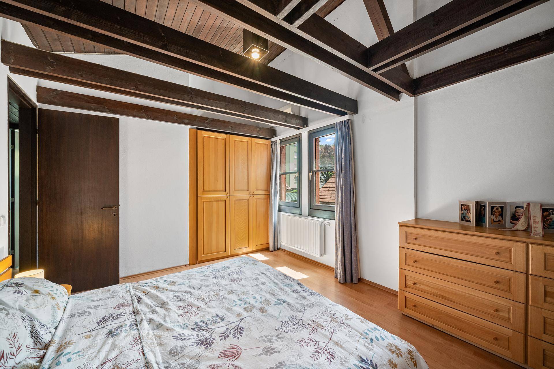 Helles Schlafzimmer mit Holzbalken, Einbauschrank und Kommode aus hellem Holz.