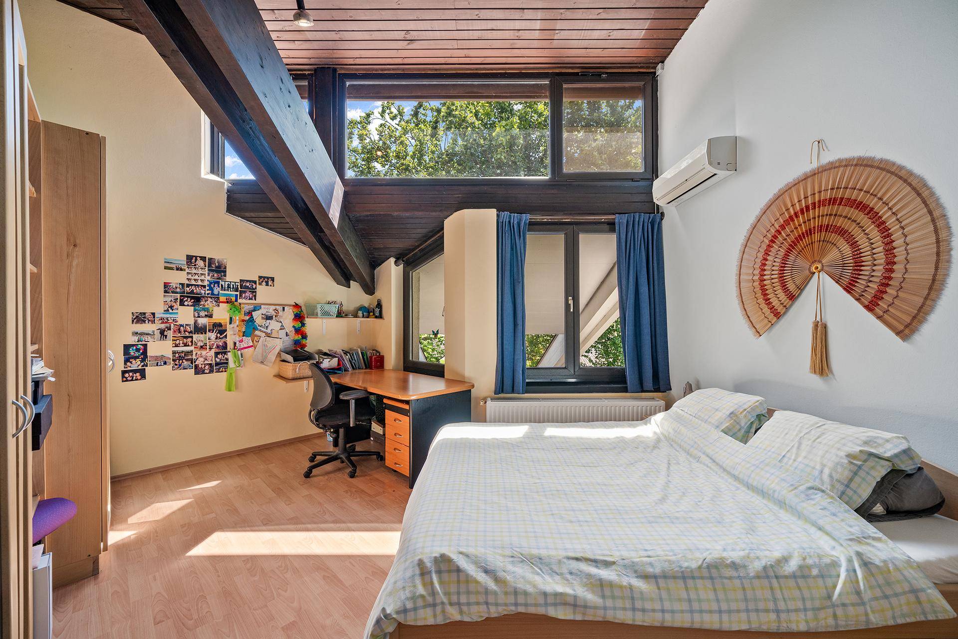 Gemütliches Schlafzimmer mit Holzbalken, Schreibtisch und Klimaanlage unter dem Dach.