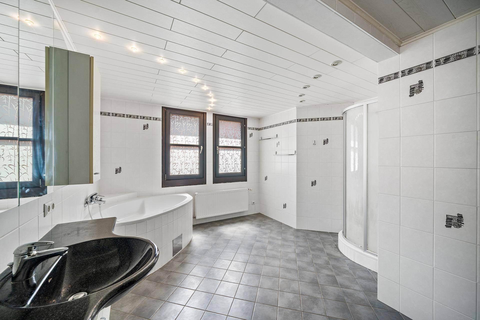 Geräumiges Badezimmer mit Badewanne, Duschkabine und zwei Fenstern.
