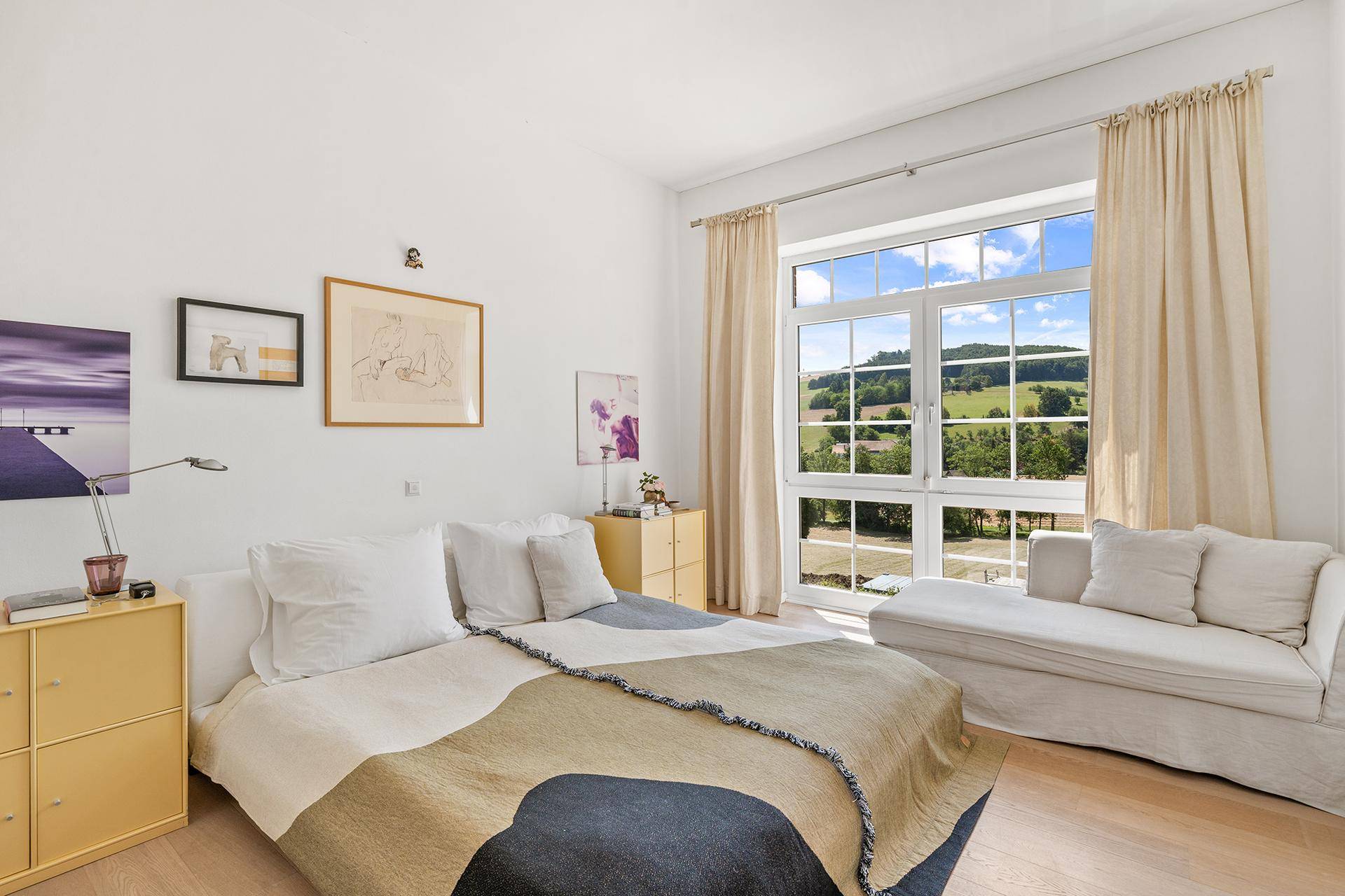 Helles Schlafzimmer mit großem Fenster, das einen weiten Blick auf die grüne Landschaft bietet.