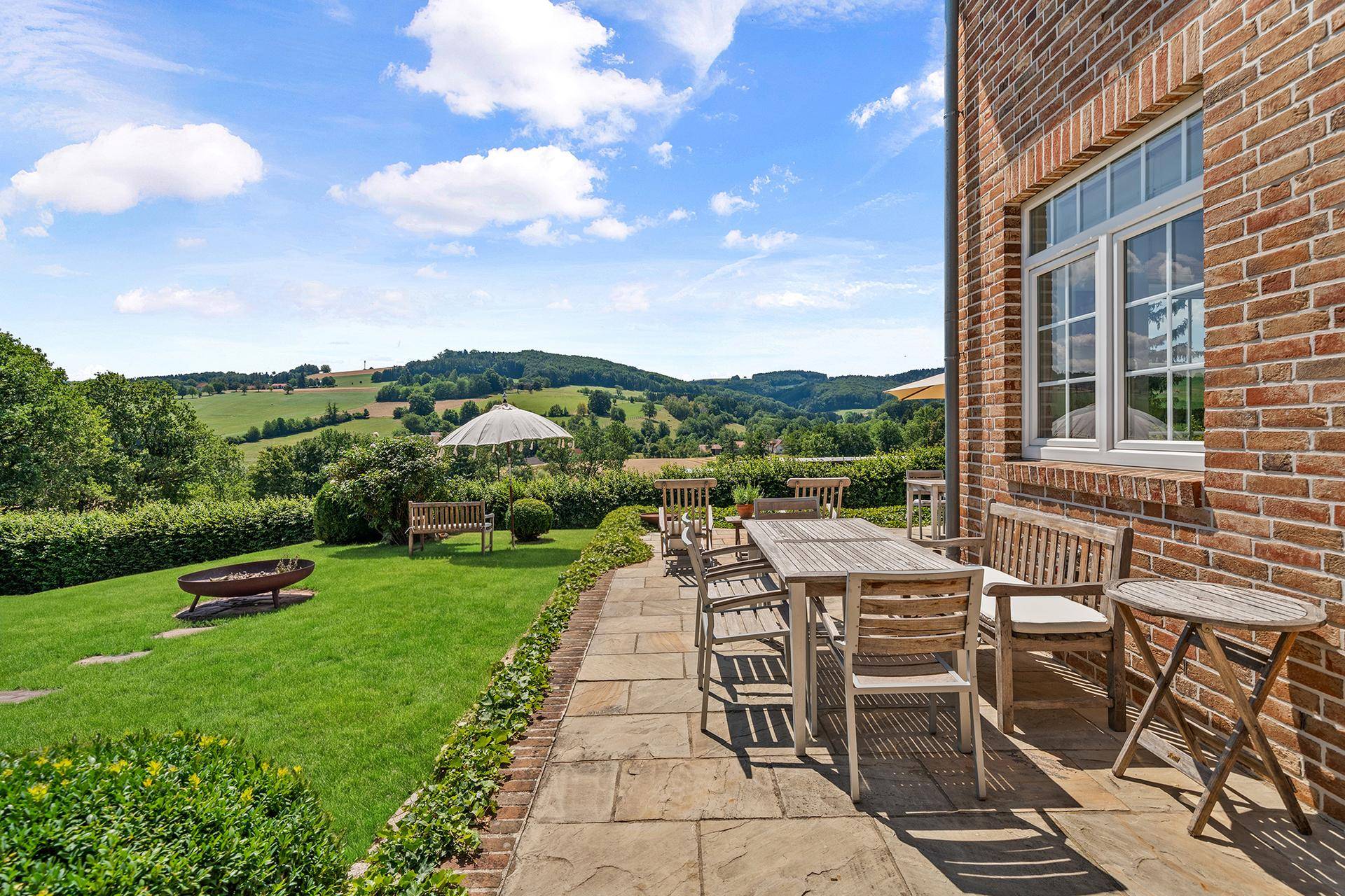 Geräumige Terrasse mit Holztisch und Stühlen, umgeben von grüner Landschaft und Hügelblick.