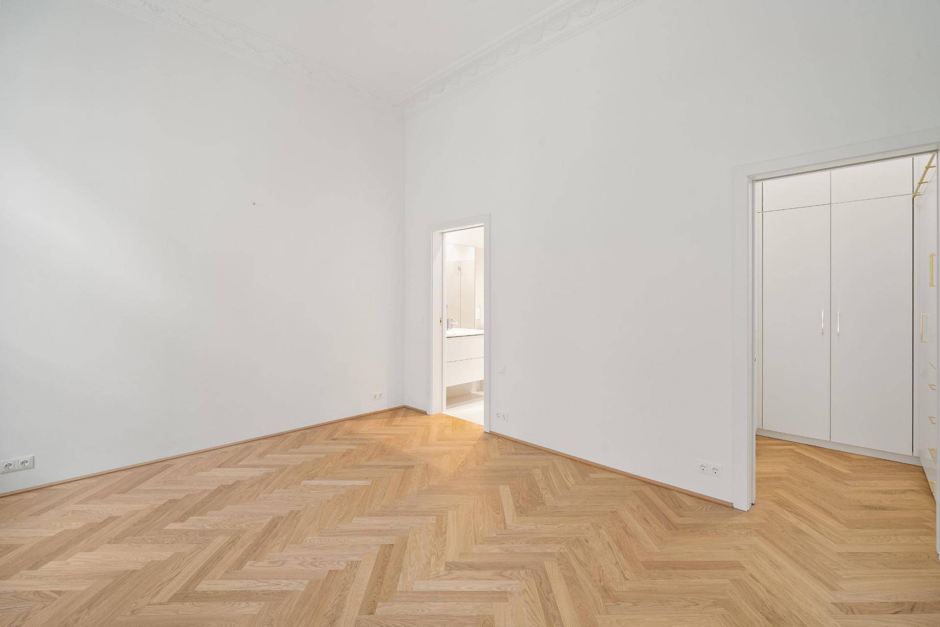 Helles Schlafzimmer mit Fischgrätparkett, Zugang zu Bad und Einbauschrank.