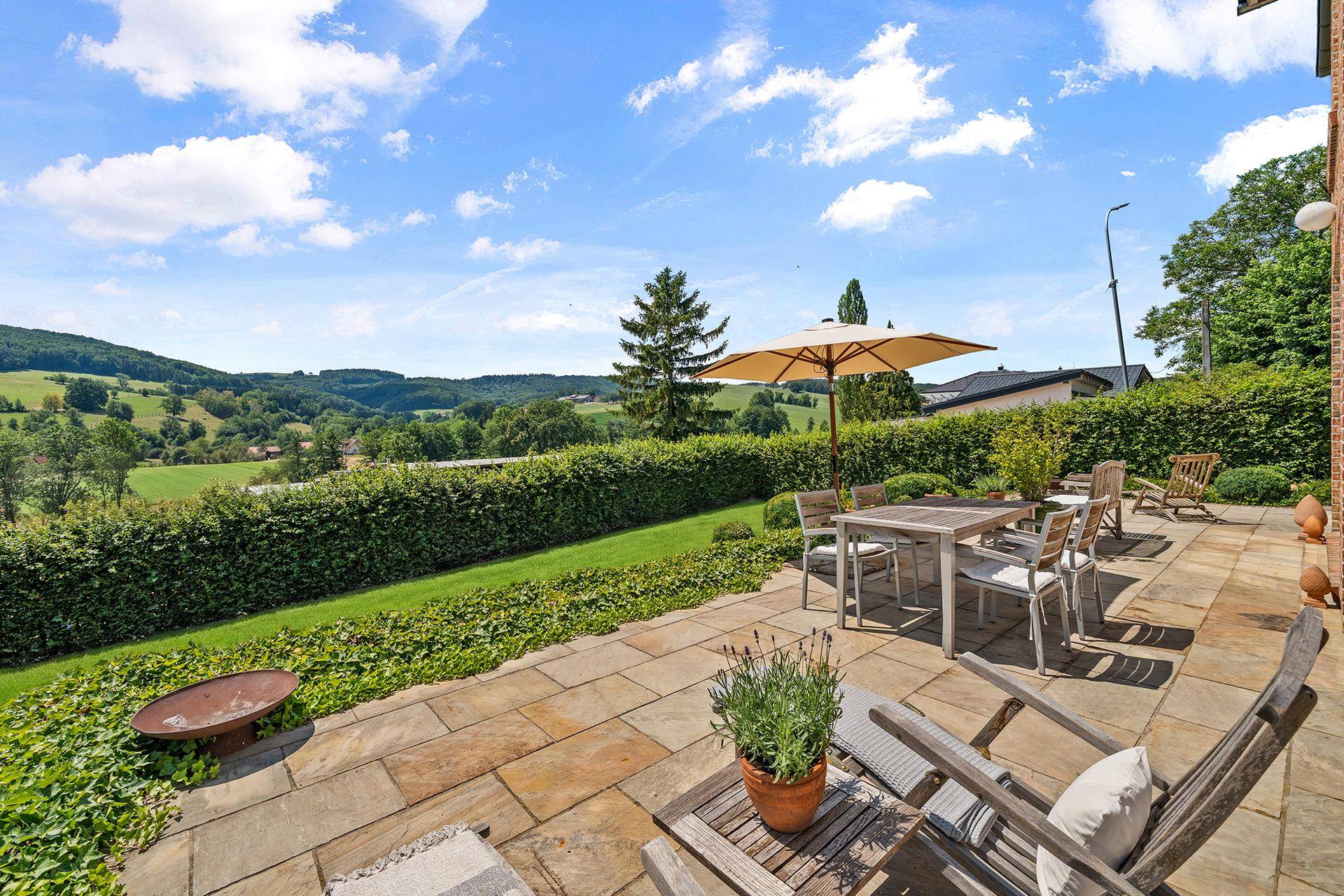 Großzügige Terrasse mit Feuerstelle und weitem Blick über die hügelige Landschaft.