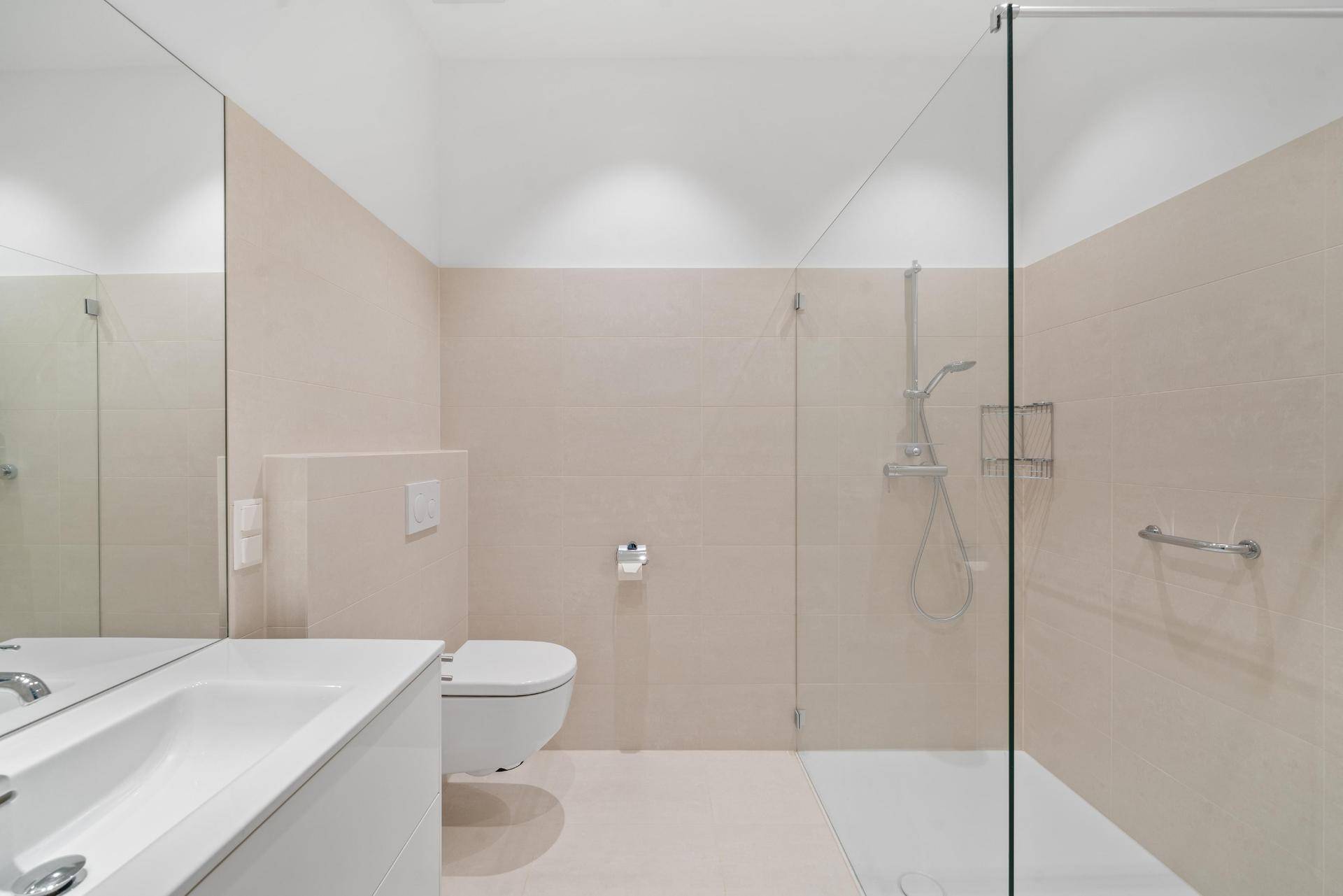 Modernes Badezimmer mit begehbarer Dusche, Wand-WC und eleganten beigen Fliesen.