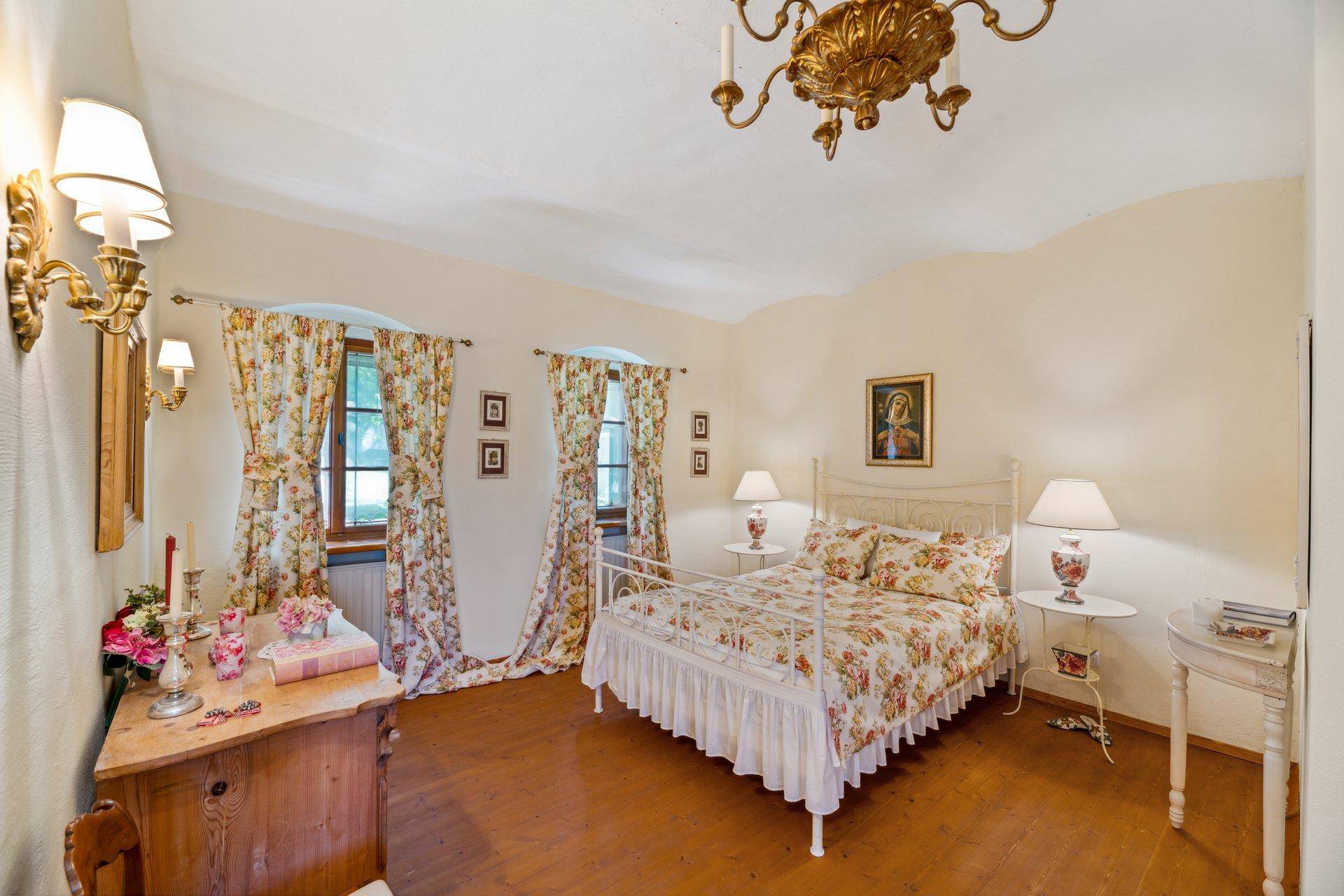 Elegantes Schlafzimmer mit floralen Vorhängen, schmiedeeisernem Bett und Holzboden.