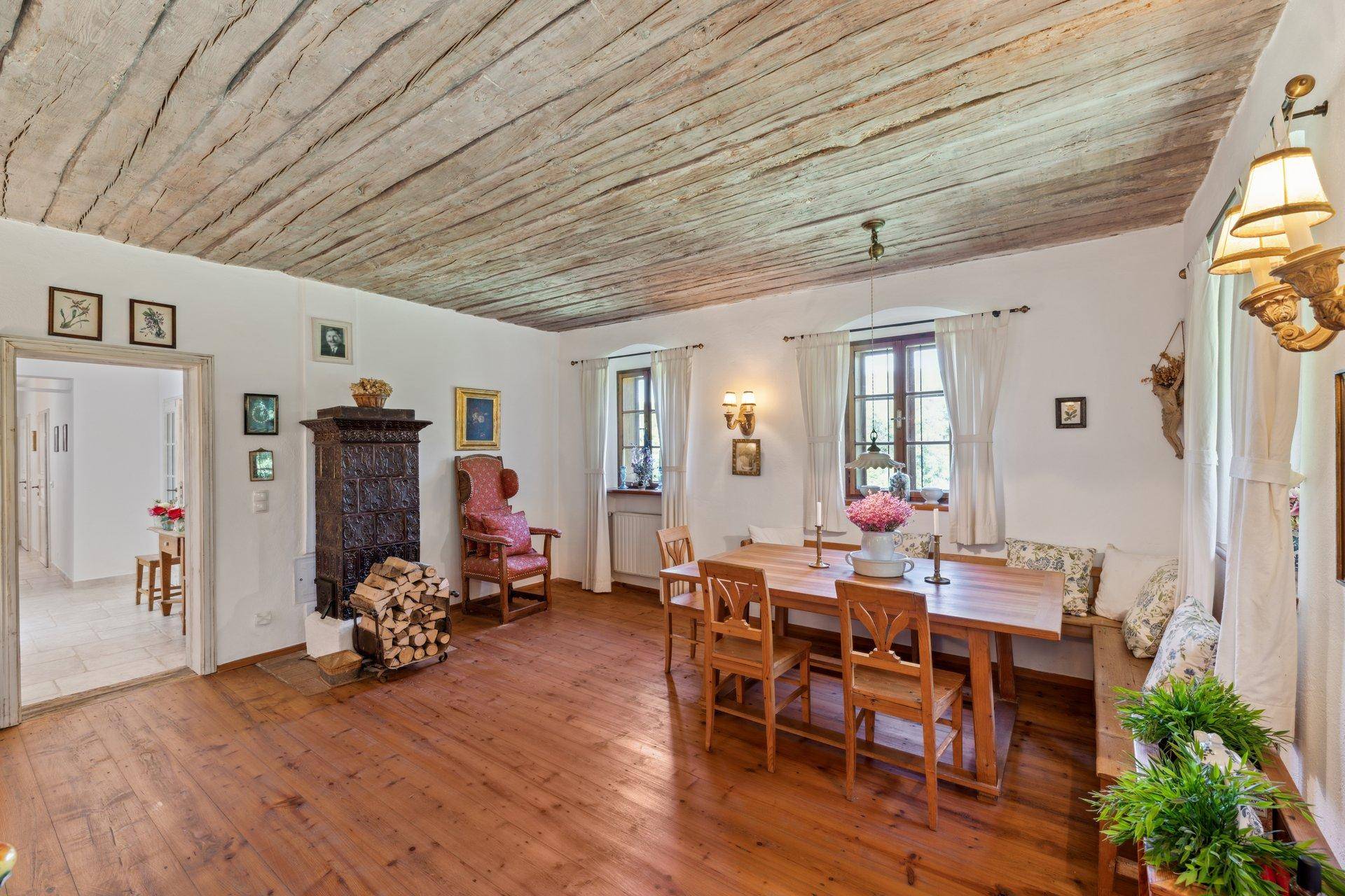 Geräumiges Esszimmer mit Holzboden, freiliegenden Deckenbalken und traditionellem Kachelofen.