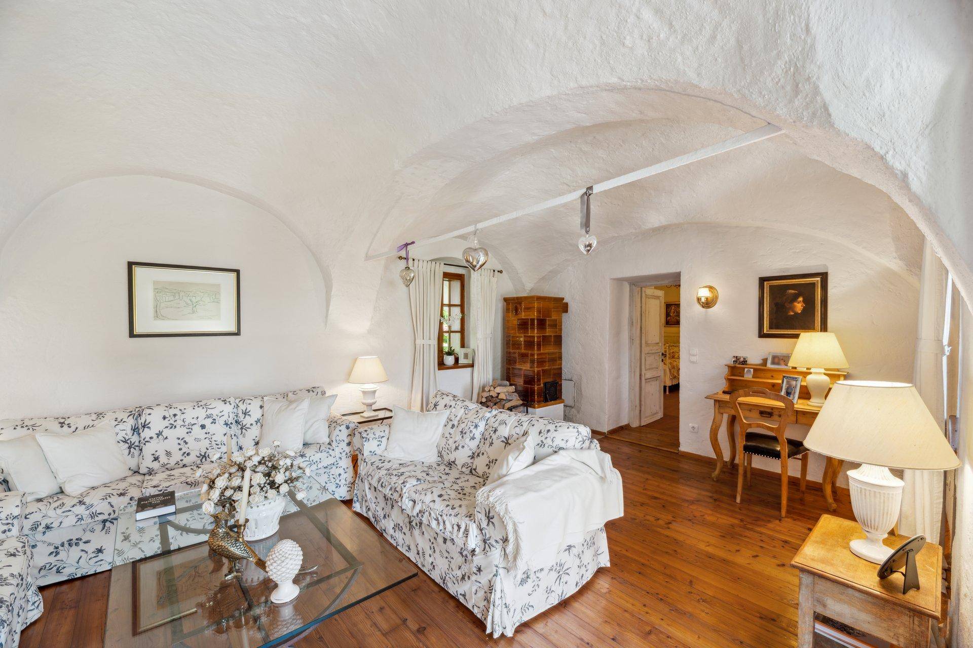 Gemütliches Wohnzimmer mit weiß getünchten Gewölbedecken, floralen Sofas und Holzboden.