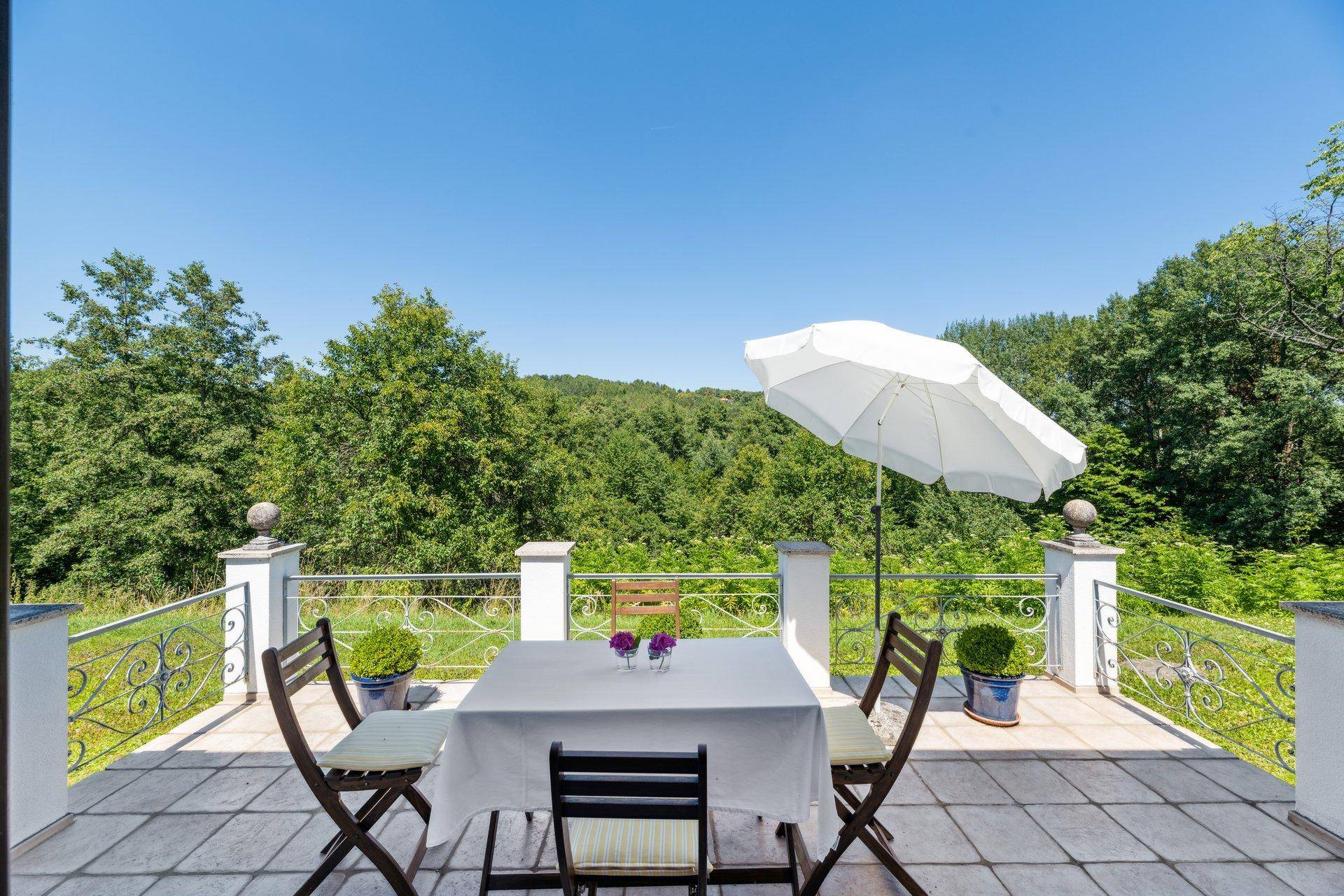 Sonniger Balkon mit Esstisch, Sonnenschirm und weitem Blick ins Grüne.