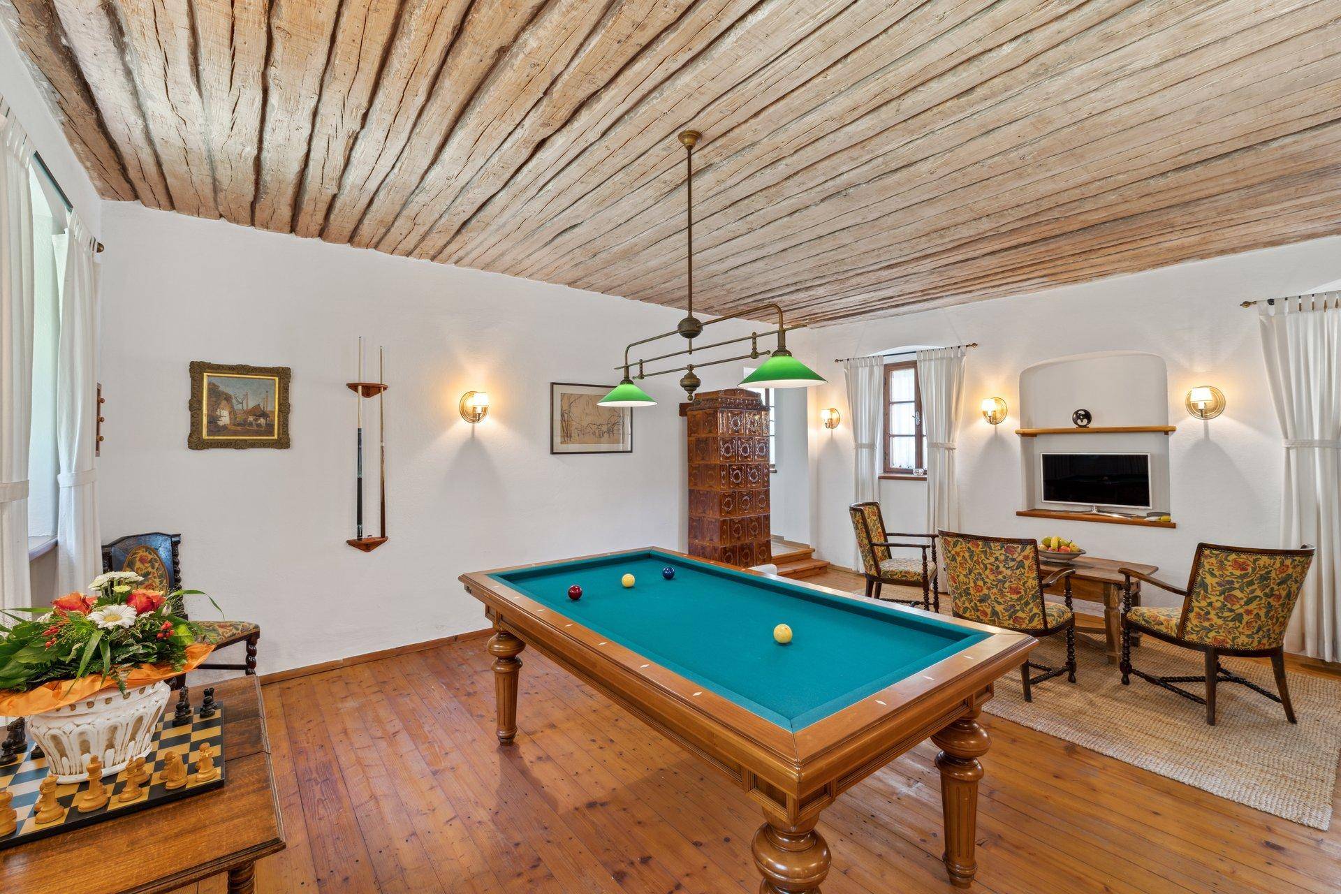 Rustikaler Spielraum mit Billardtisch, freiliegenden Holzbalken und traditionellem Kachelofen.