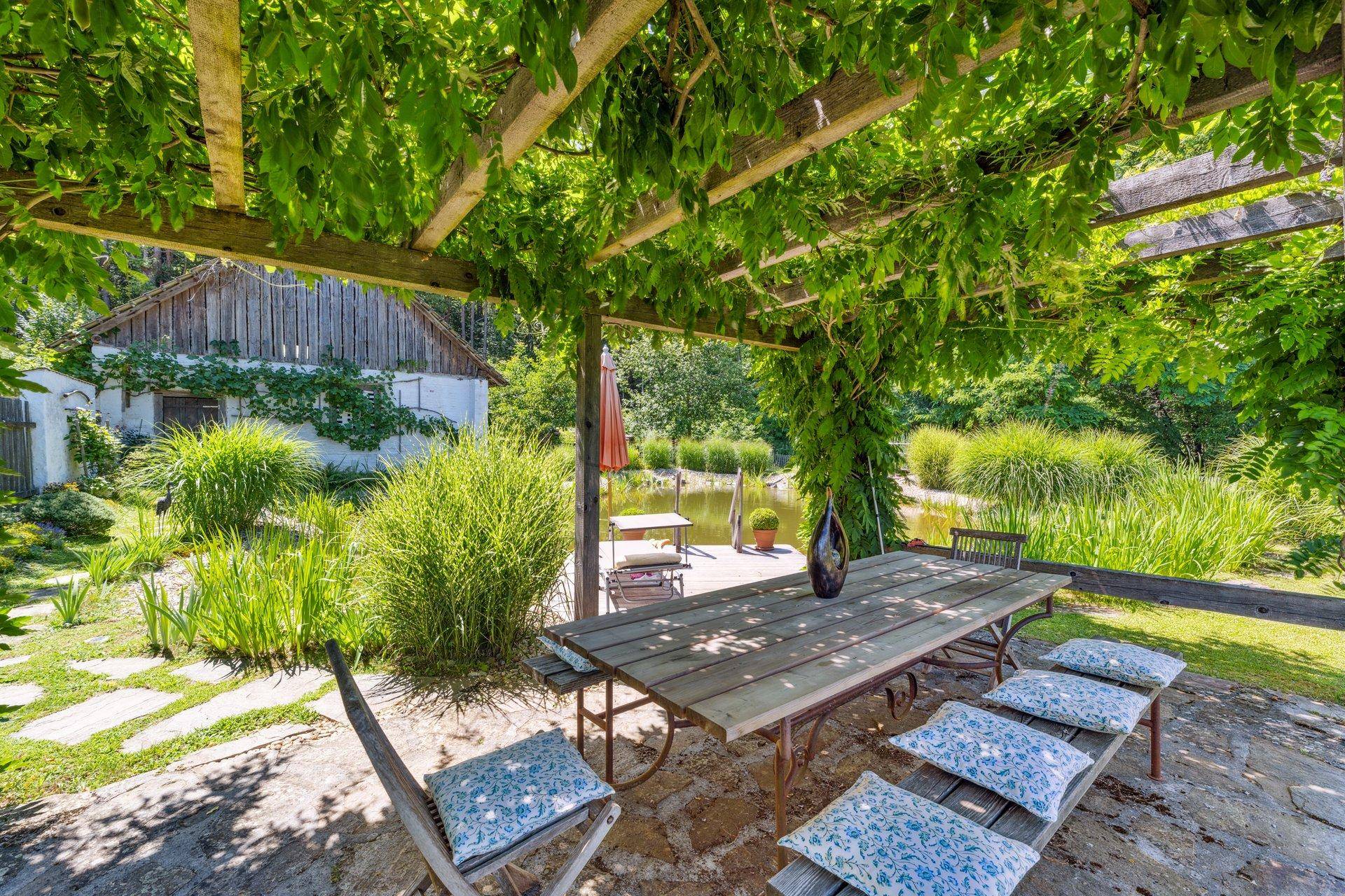 Überdachter Essbereich im Freien unter einer Pergola mit Blick auf den Teich.